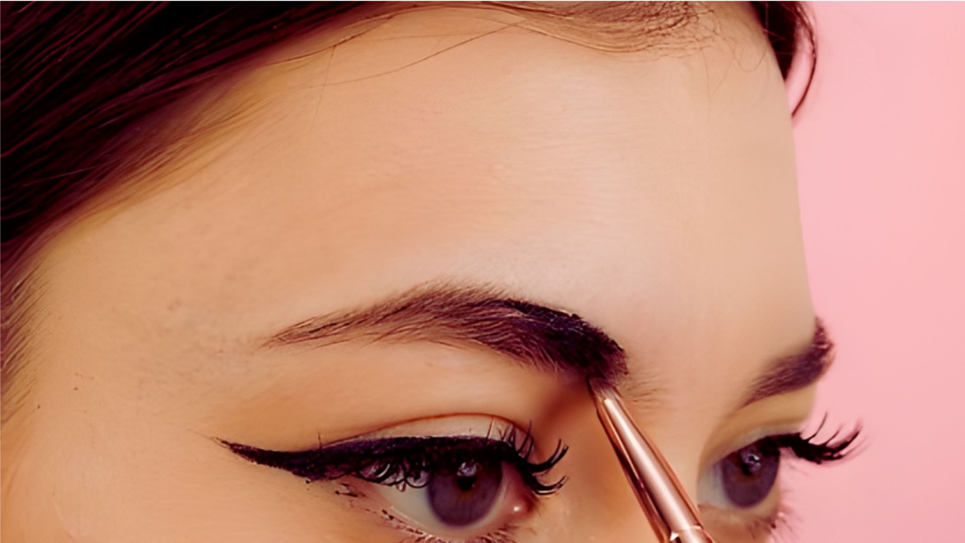 A woman with long eyelashes applies dark tinted eyebrow fixing with a brush.