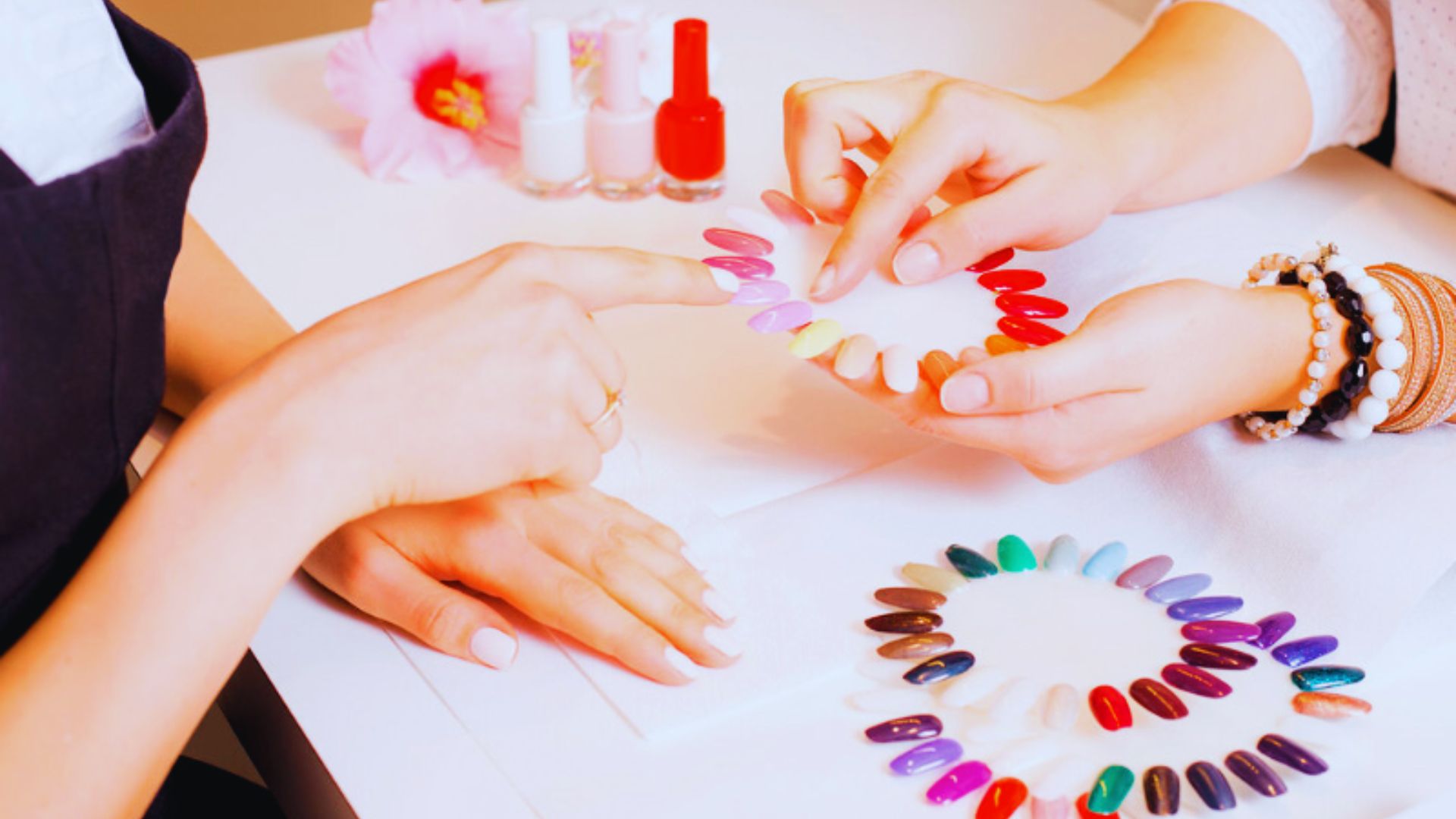 A woman enjoys a manicure, with a nail technician carefully applying vibrant nail polish to her nails in a salon setting.