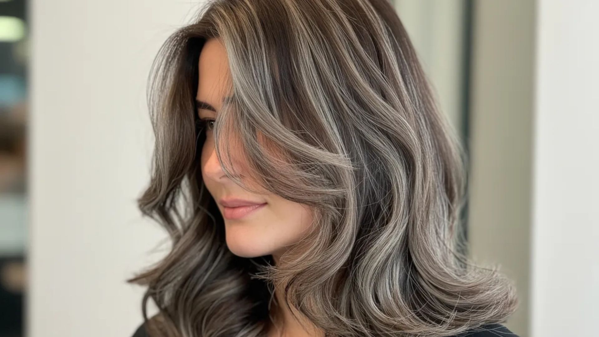 A woman with long, wavy hair featuring gray highlights, elegantly framing her face.