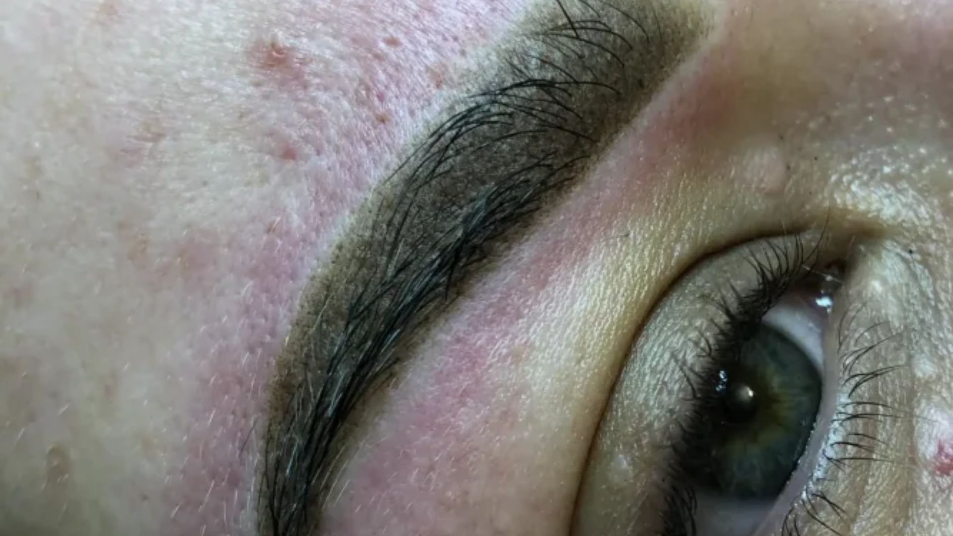 A close-up of a woman's eye featuring a detailed tattoo around the eyelid, showcasing intricate designs and colors.