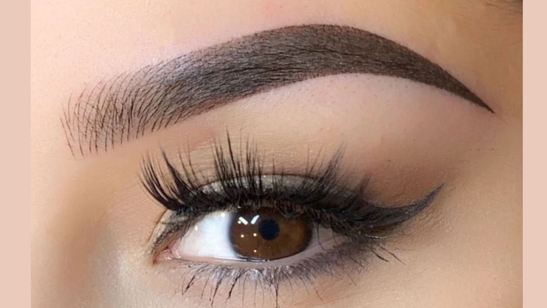 Detailed view of a woman's eye with a prominent, long eyebrow framing the eye.