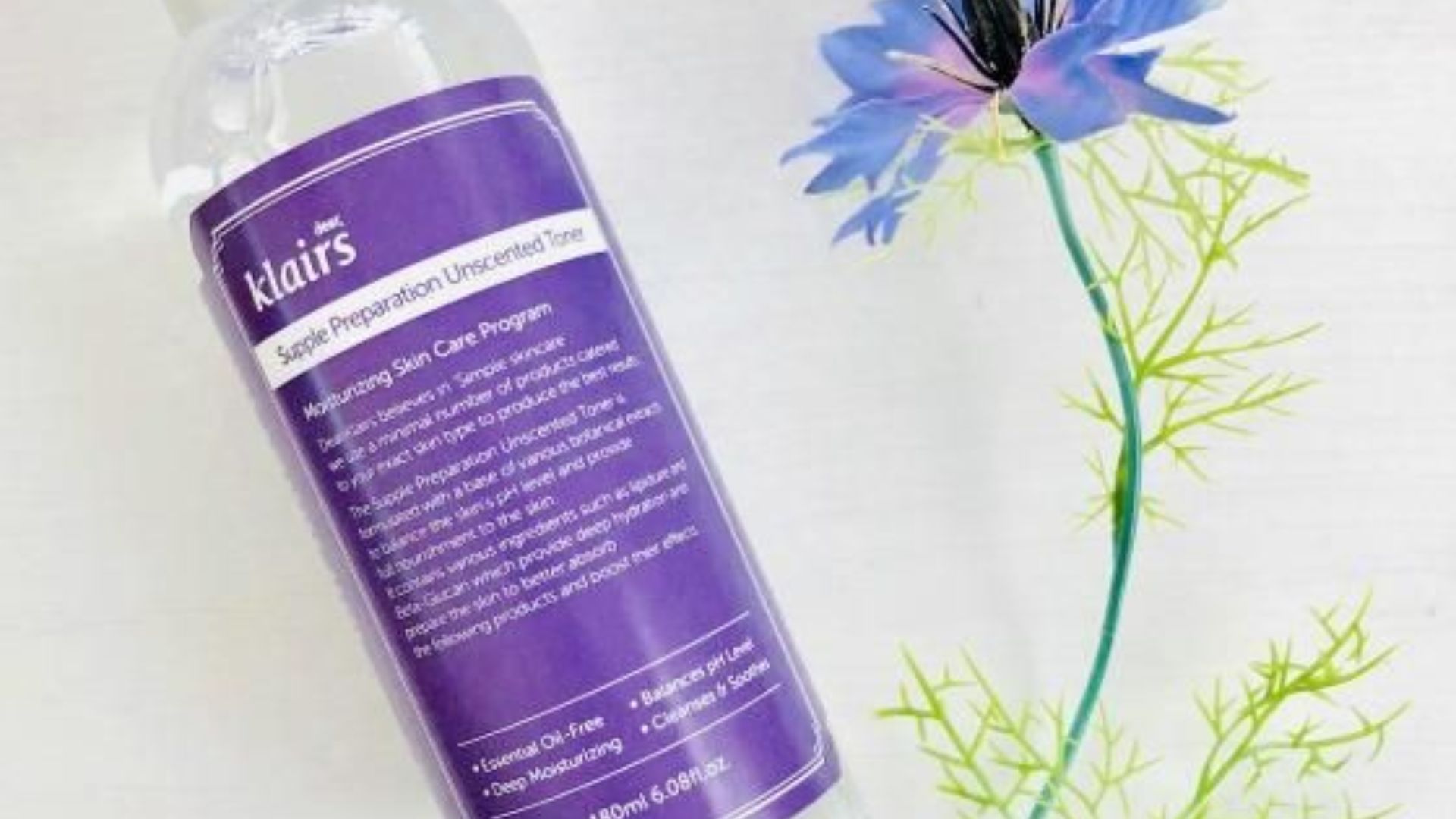 A clear bottle of water placed beside a vibrant flower on a neutral background.