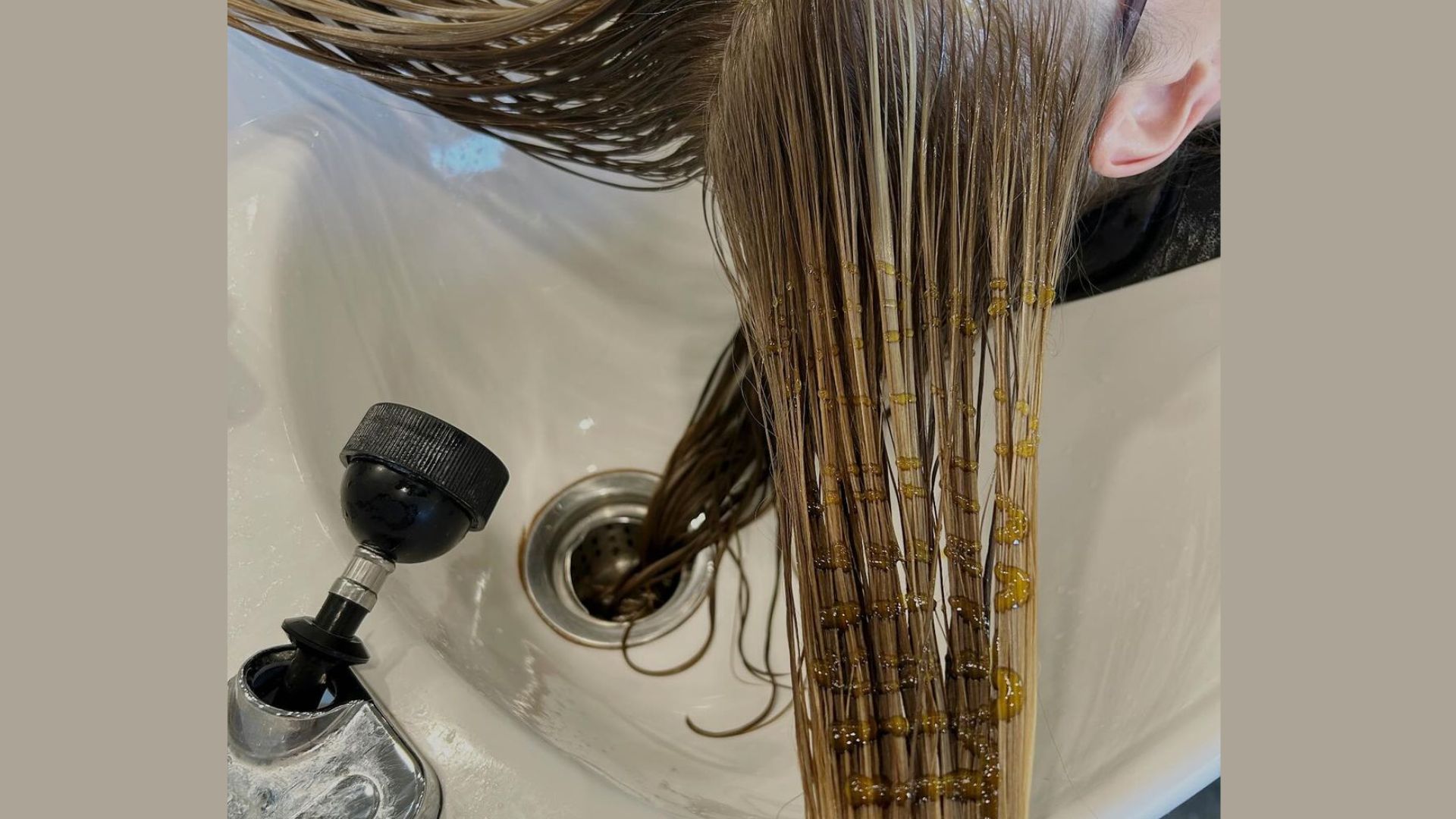 A woman is washing her hair in a sink, with water flowing and shampoo lathering in her hair.