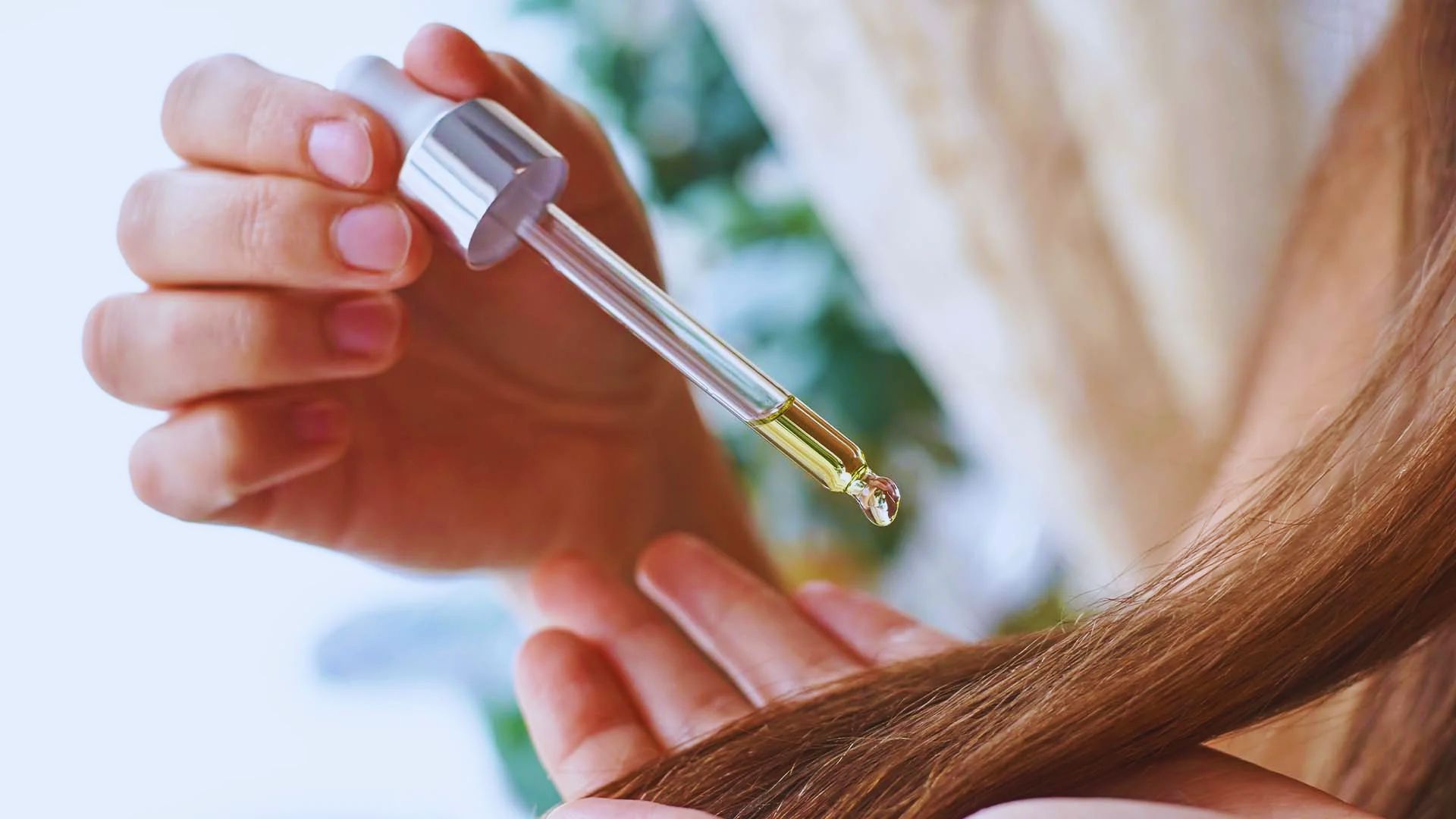 A woman applies castor oil to her long hair, focusing on nourishing and enhancing its shine and health.
