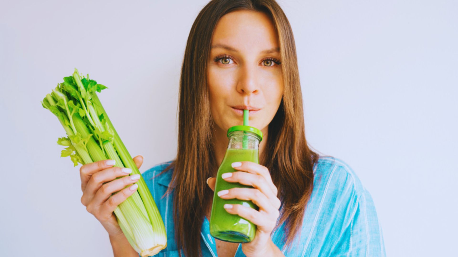 A woman holds a green drink alongside fresh celery, emphasizing its benefits for skin health.