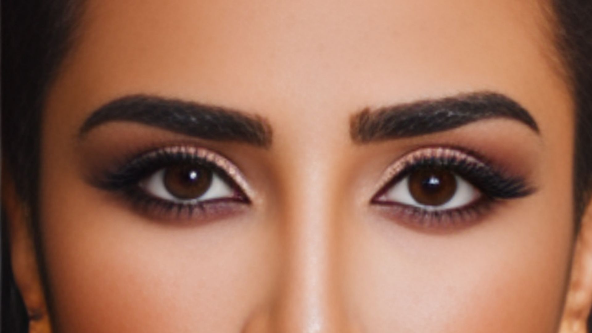 Close-up of a woman with large eyes and a notable nose, emphasizing her dark tinted eyebrows.