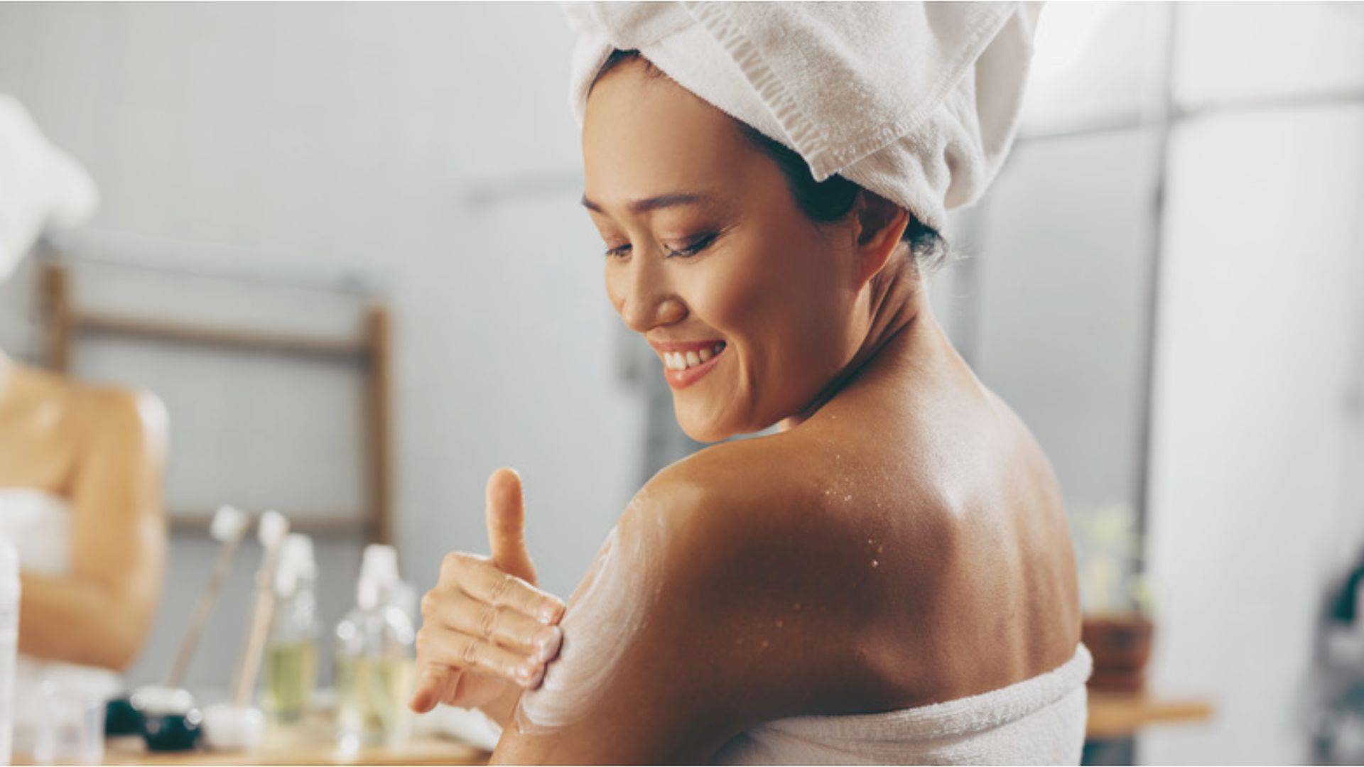 A woman smiles as she applies her skincare products, showcasing a joyful and self-care moment