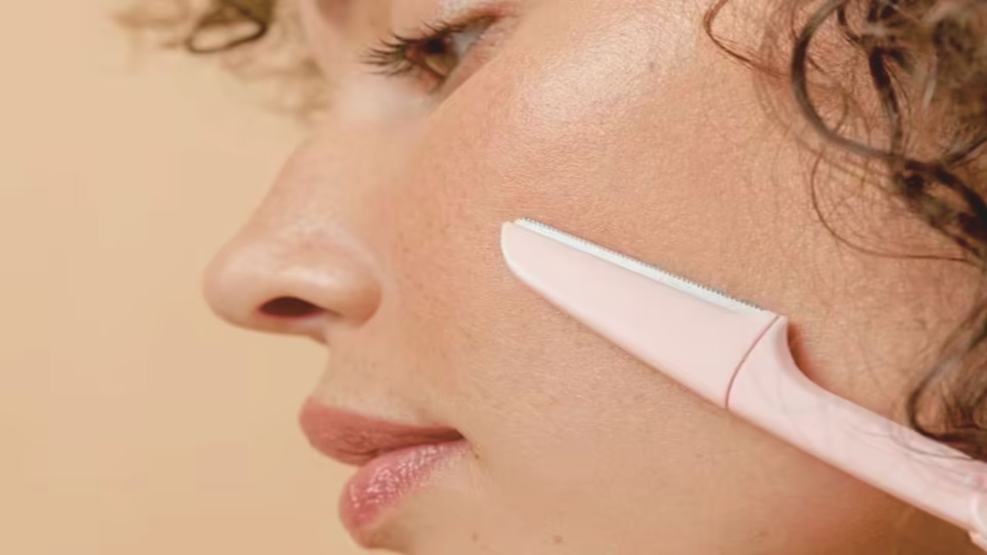 A woman cleans her face with a pink toothbrush, demonstrating a unique skincare routine.