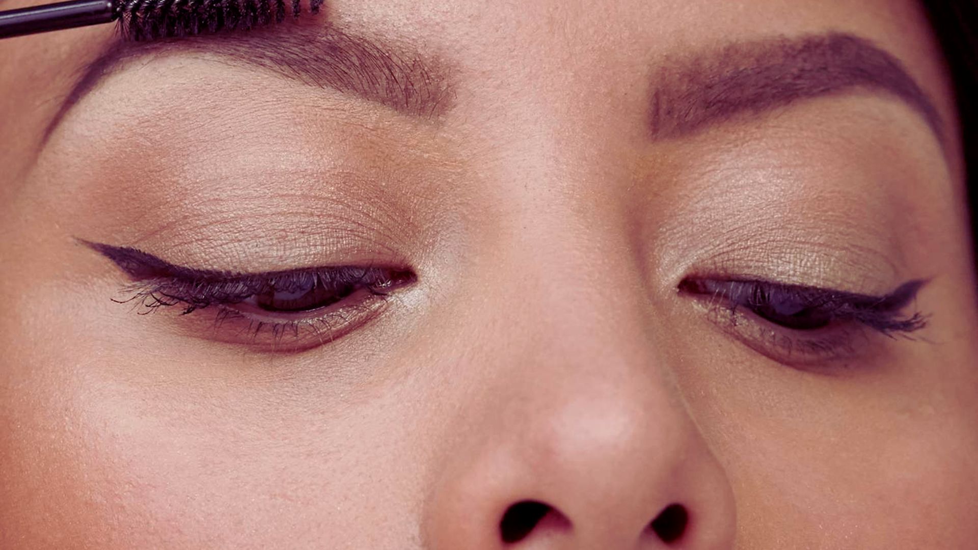 A woman carefully applies mascara to her eyebrows, upgrading their shape and color with focused attention