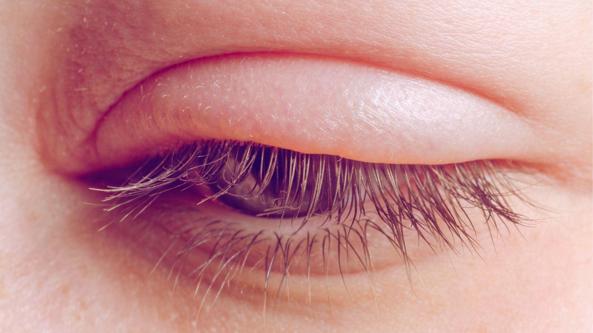 Close-up of a woman's eye, showcasing a large iris and detailed eyelashes against a soft background.