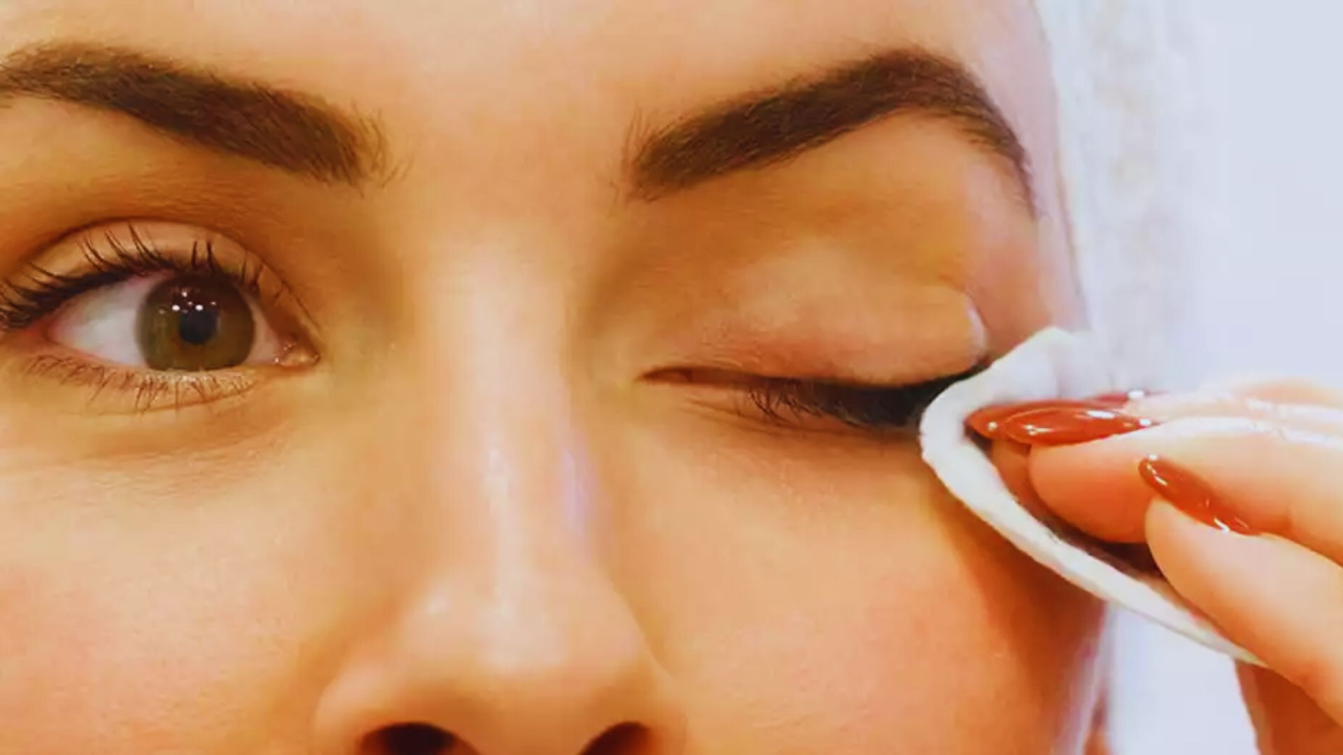 A woman gently applies a makeup wipe to her eye, removing makeup with care and focus.