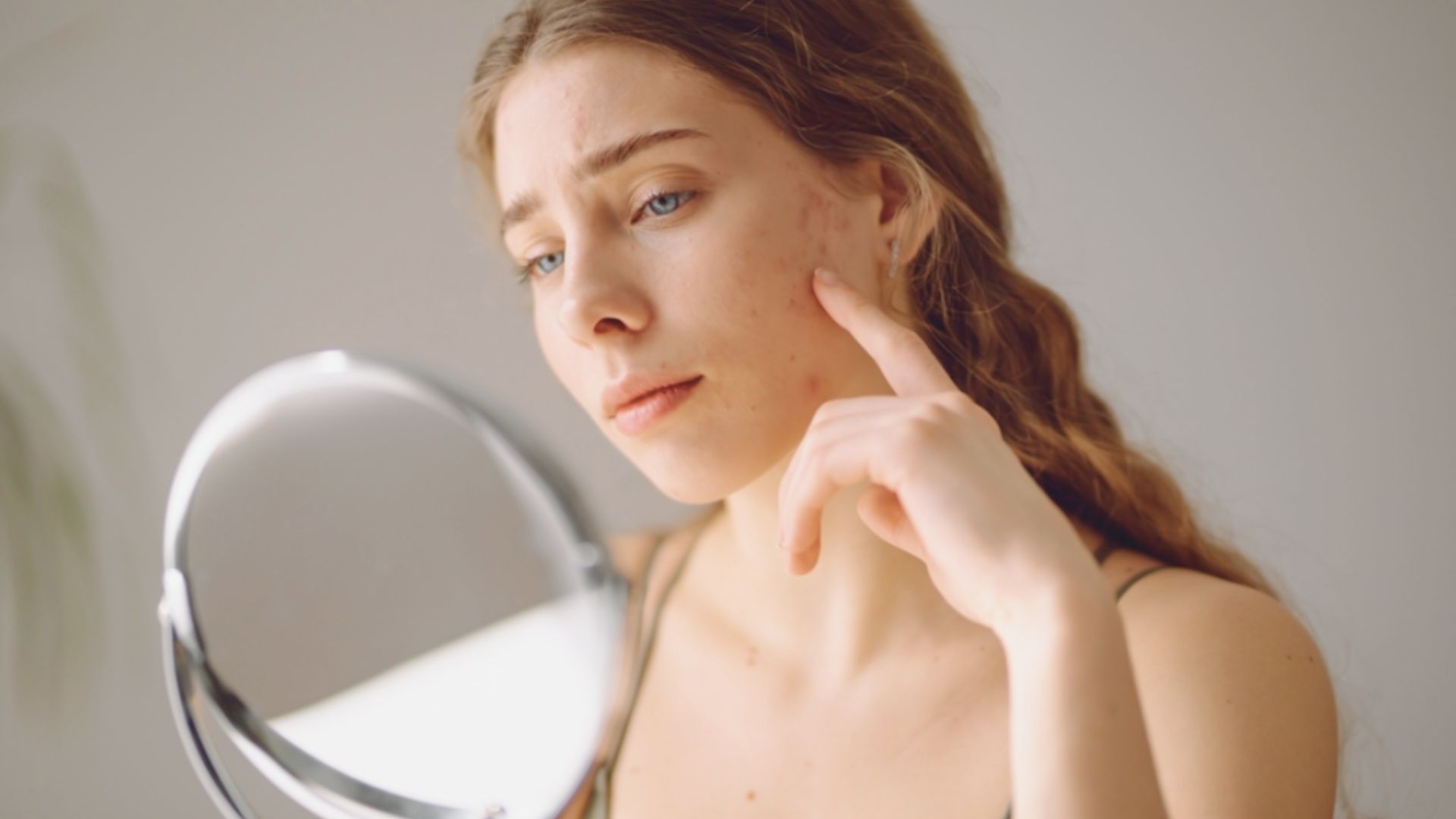A woman gazes into a mirror, her face reflected clearly, contemplating her appearance and skincare concerns.