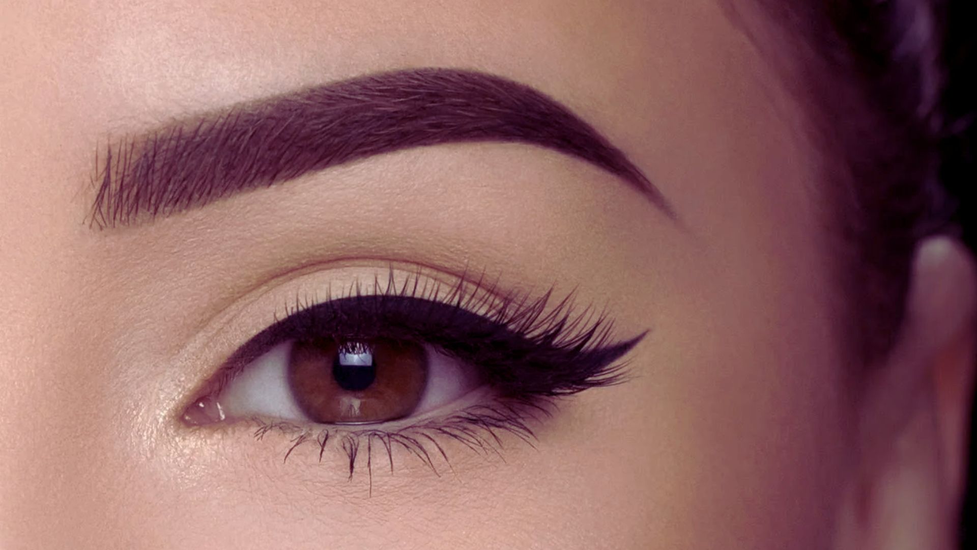 Detailed view of a woman's eye featuring a soft brown eye shadow, highlighting her eyelashes and brow.