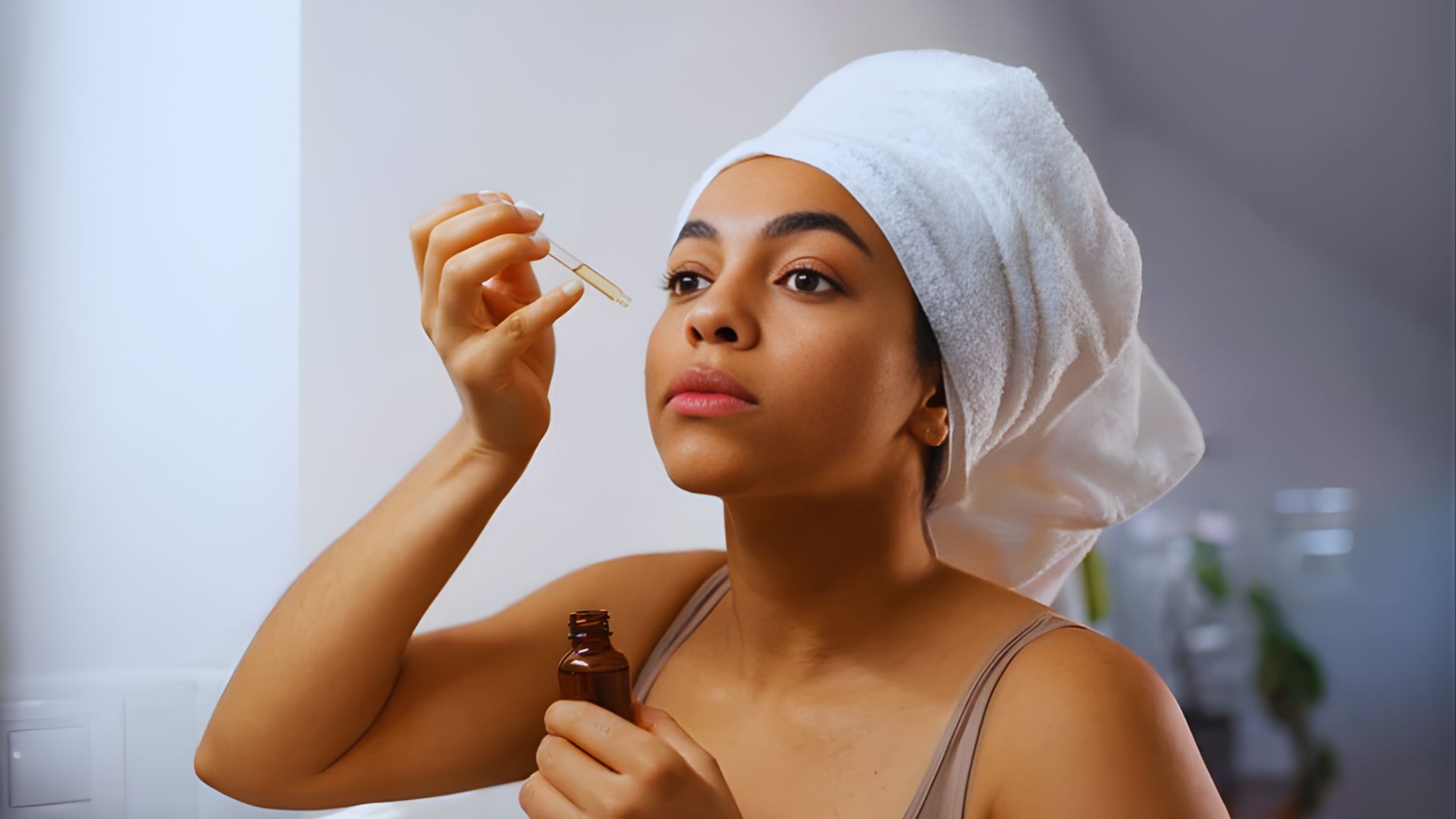 A woman wrapped in a towel holds a bottle of oil, suggesting a moment of self-care or beauty routine.