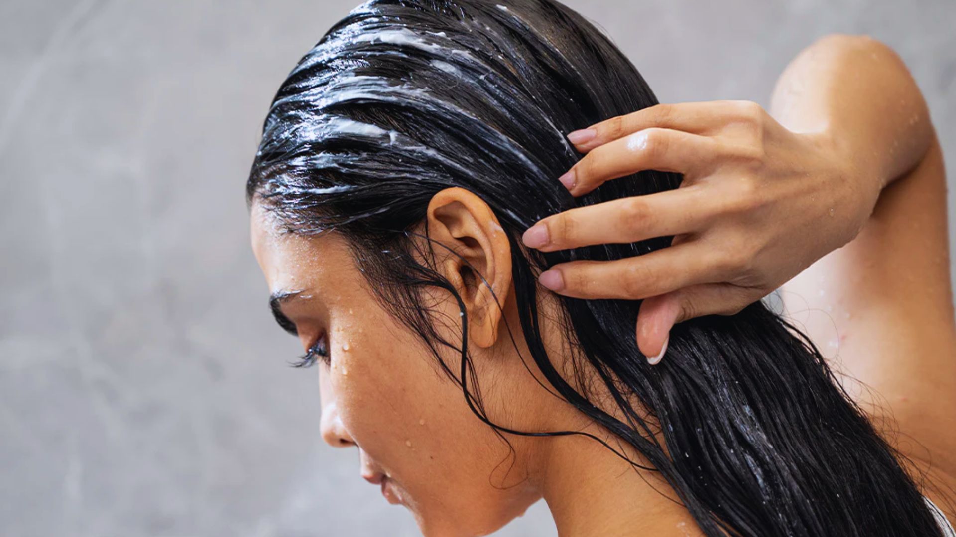 A woman washes her hair with a brush, focusing on her hair care routine in a bright bathroom setting.