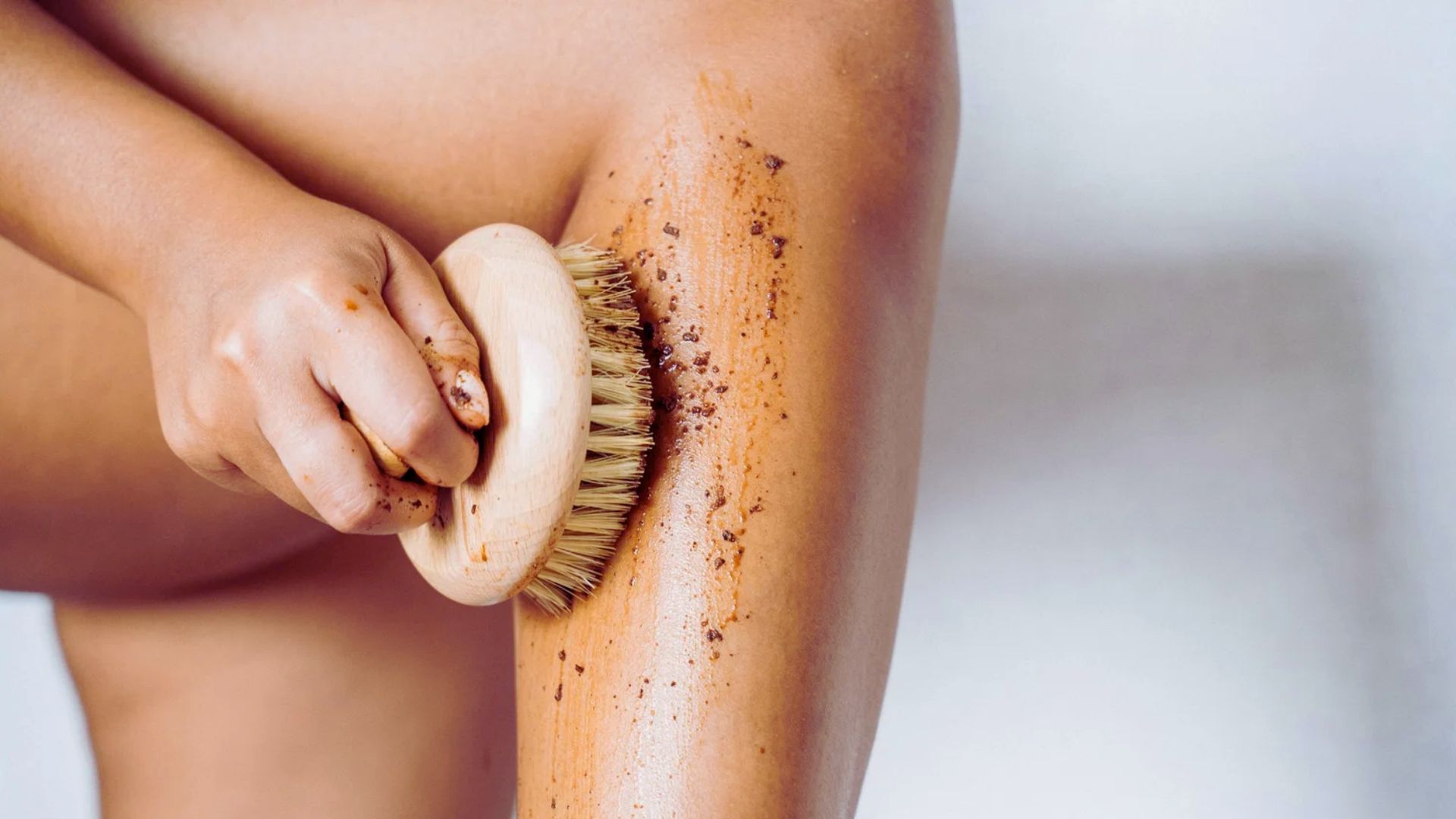 A woman brushes her legs, demonstrating a tan exfoliating technique for smoother skin.