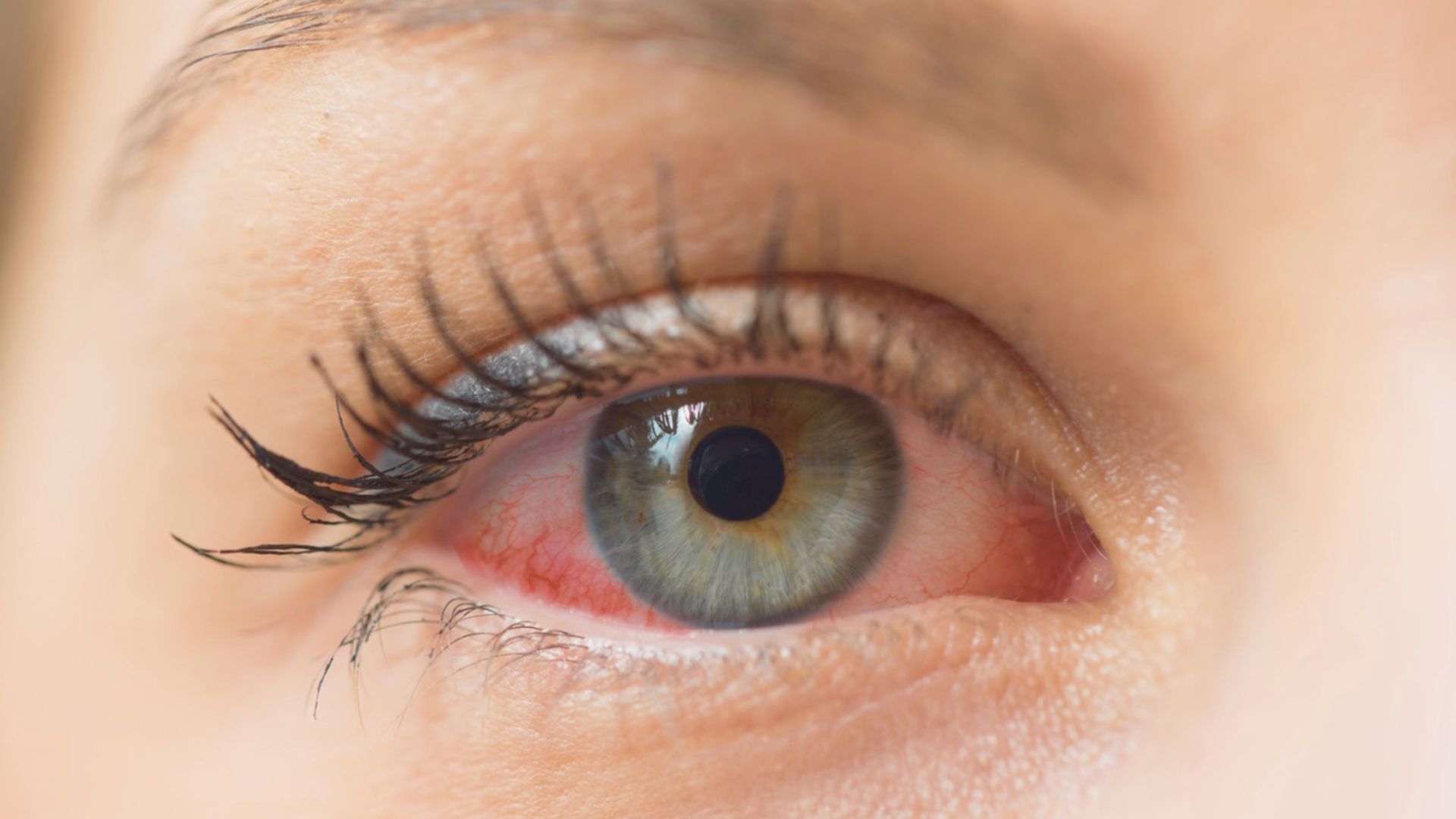 A woman with striking red eyes and one pink eye, gazing directly at the viewer with an intense expression.