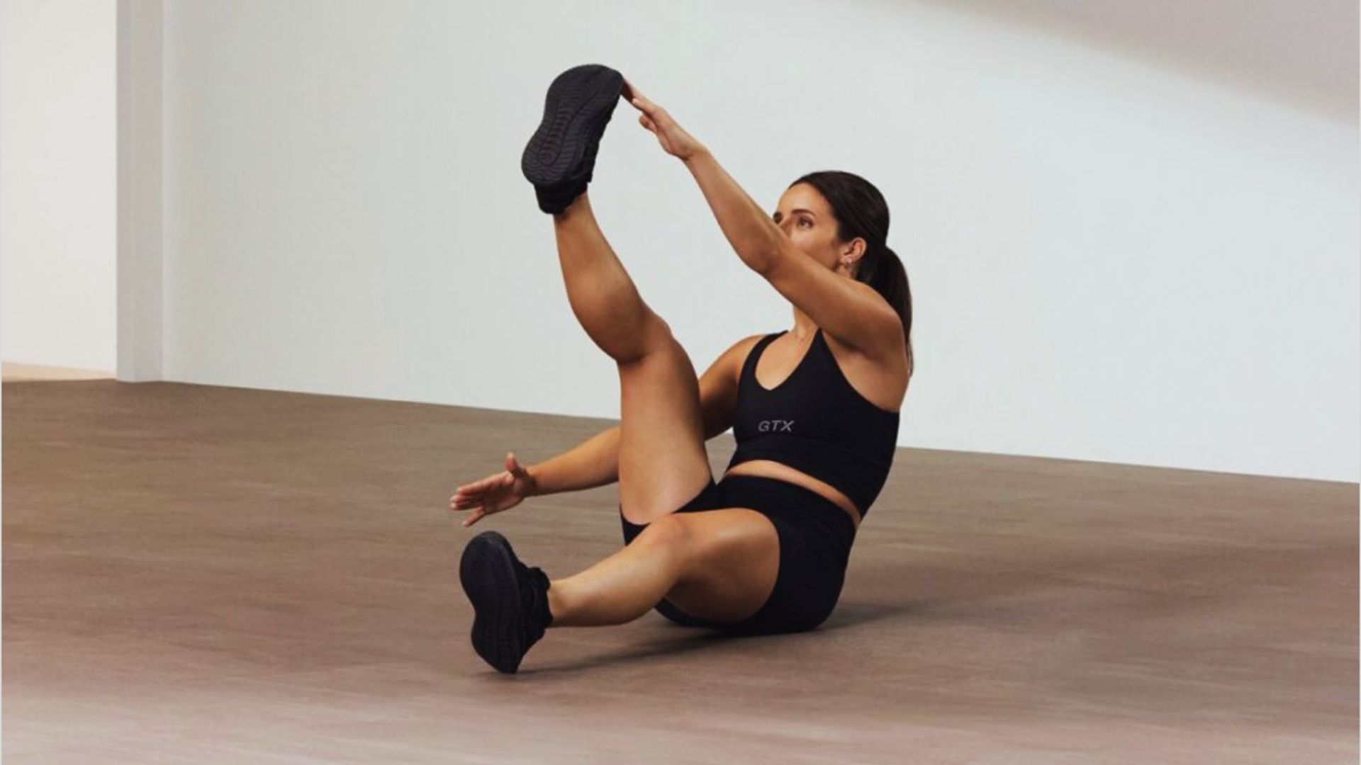 A woman performs a leg stretch in a bright studio, focusing on her flexibility and balance.