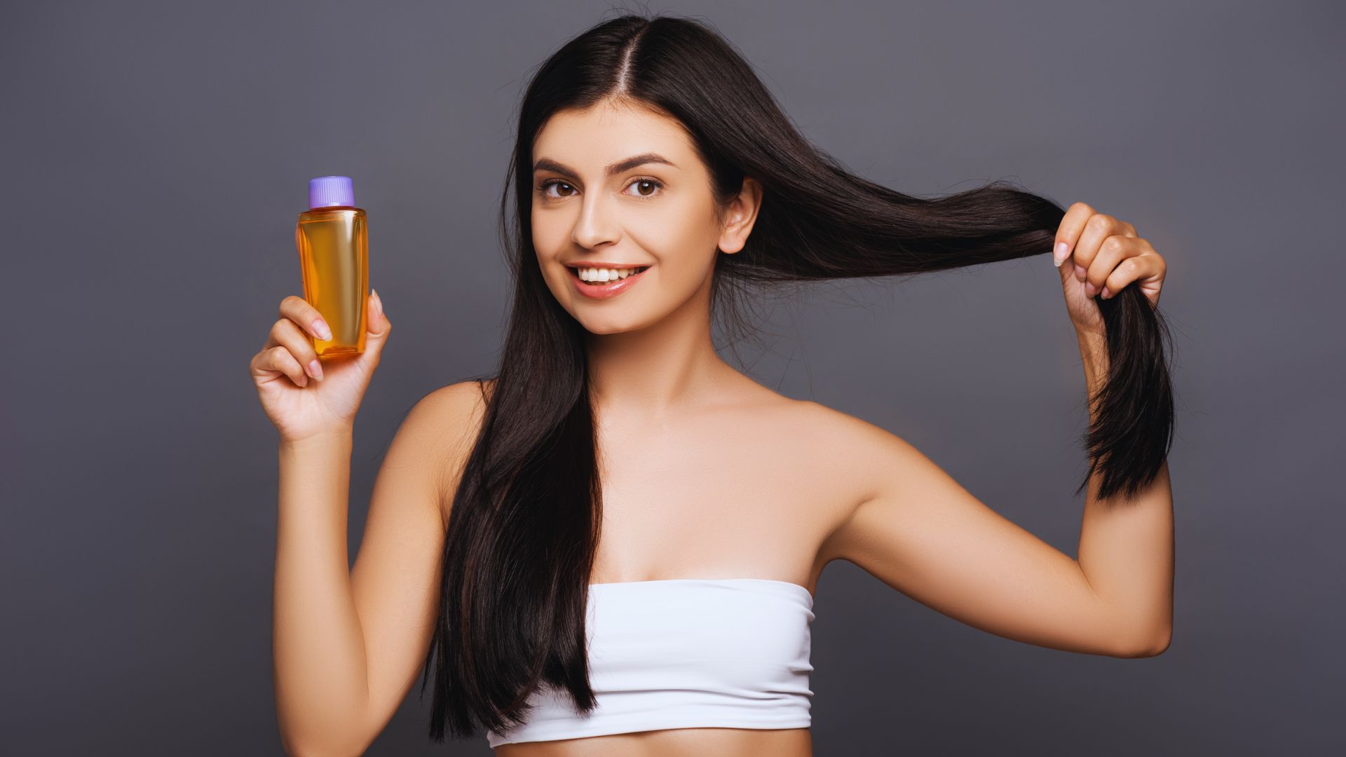 A woman holds a bottle of hair oil, showcasing its sleek design and promoting healthy hair care.