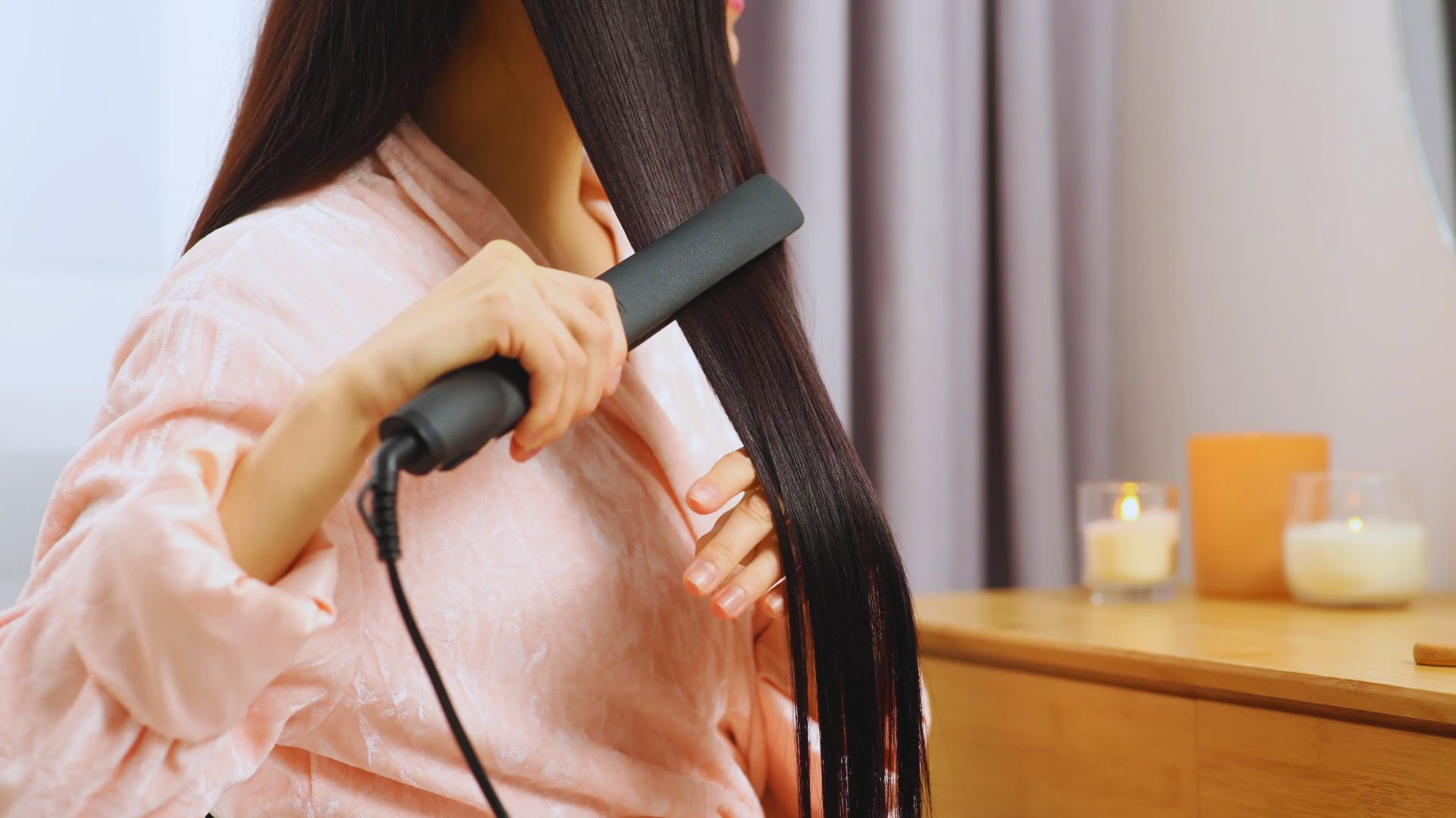 A woman straightens her hair with a hair straightener, focusing intently on achieving a sleek look.