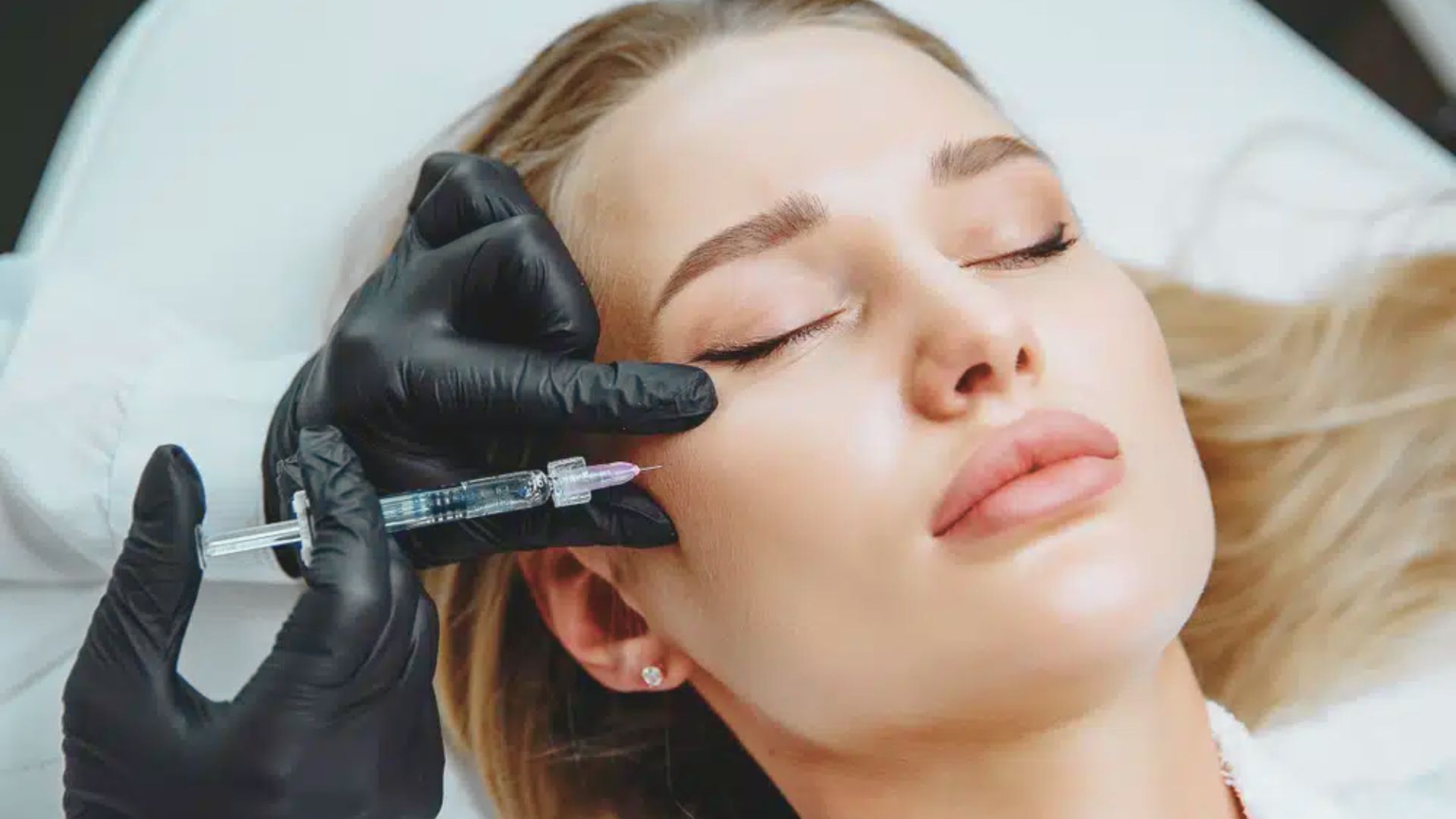 A woman receiving a facial injection at a beauty salon, with a practitioner administering the treatment.