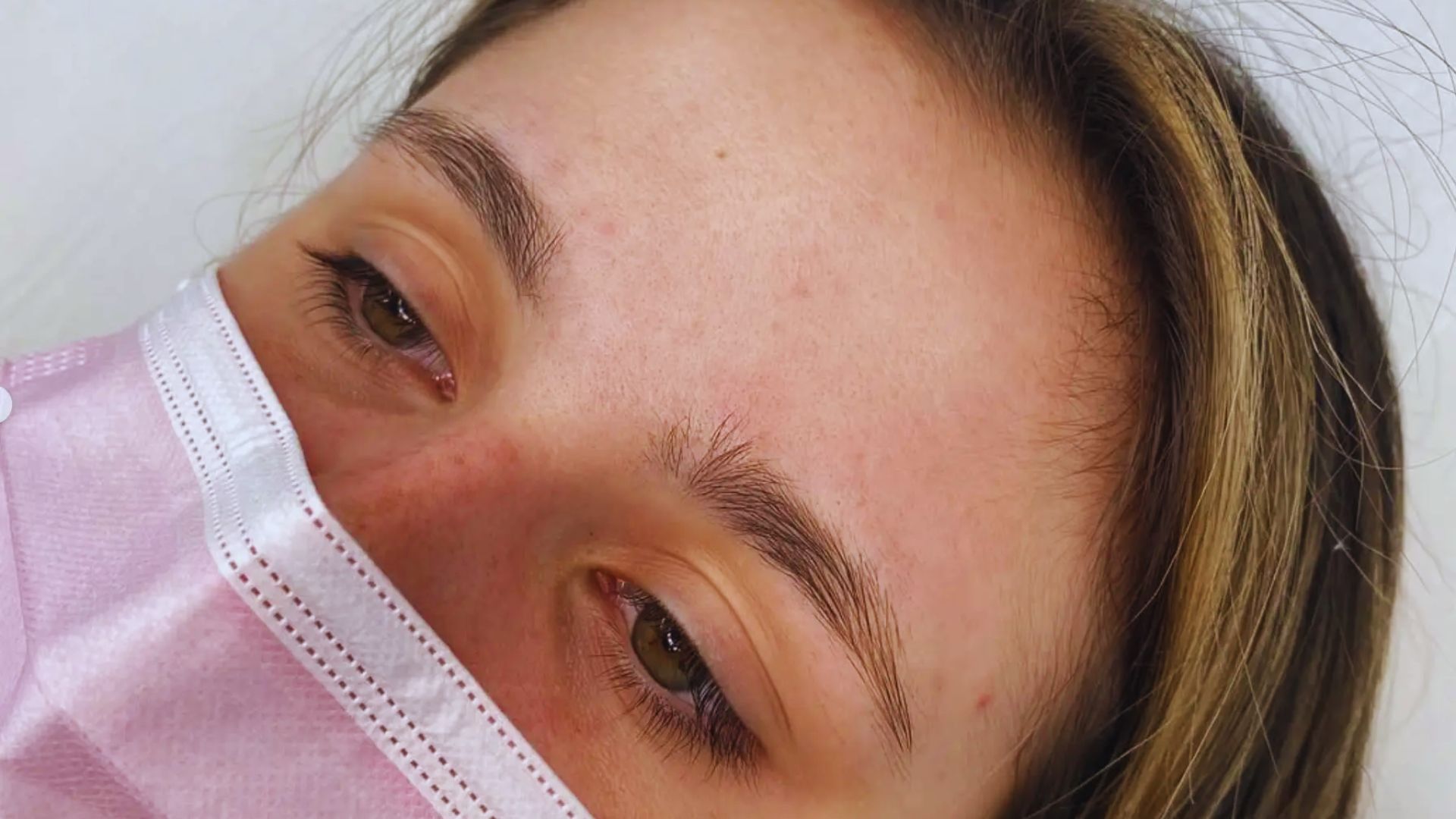 A woman wearing a surgical mask, looking directly at the camera with a neutral expression.