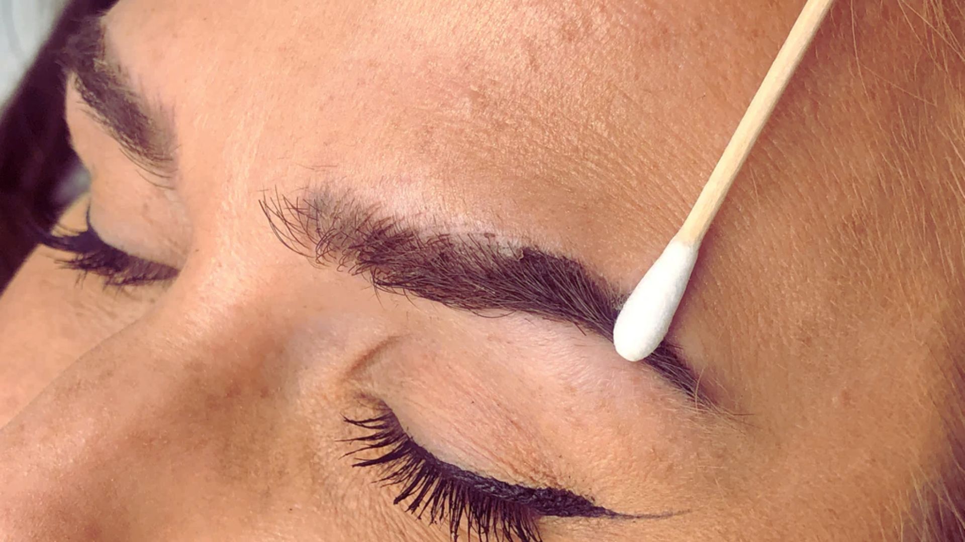A woman with a white stick resting on her eyebrow, showcasing artistic expression.