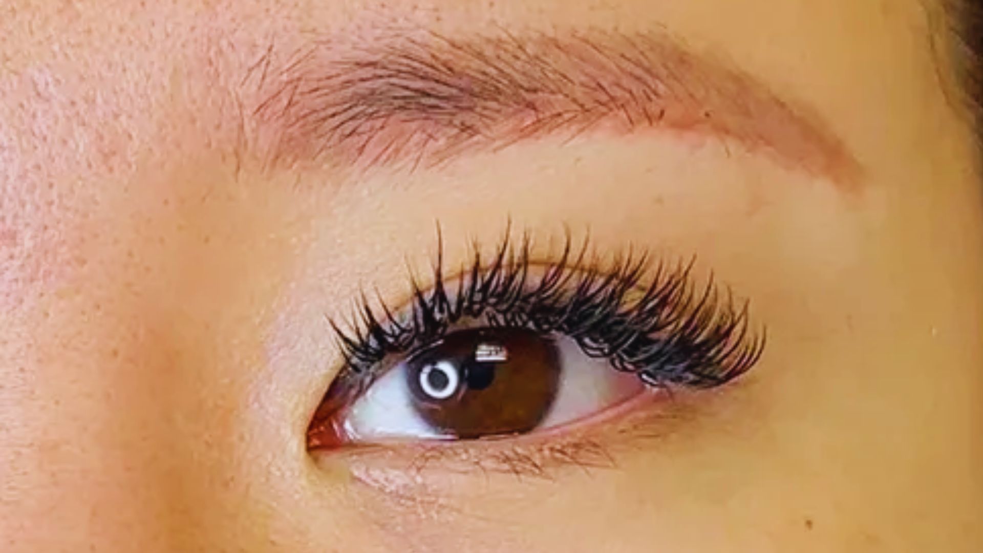 A close-up of a woman's eye showcasing long, elegant eyelashes against a soft background.