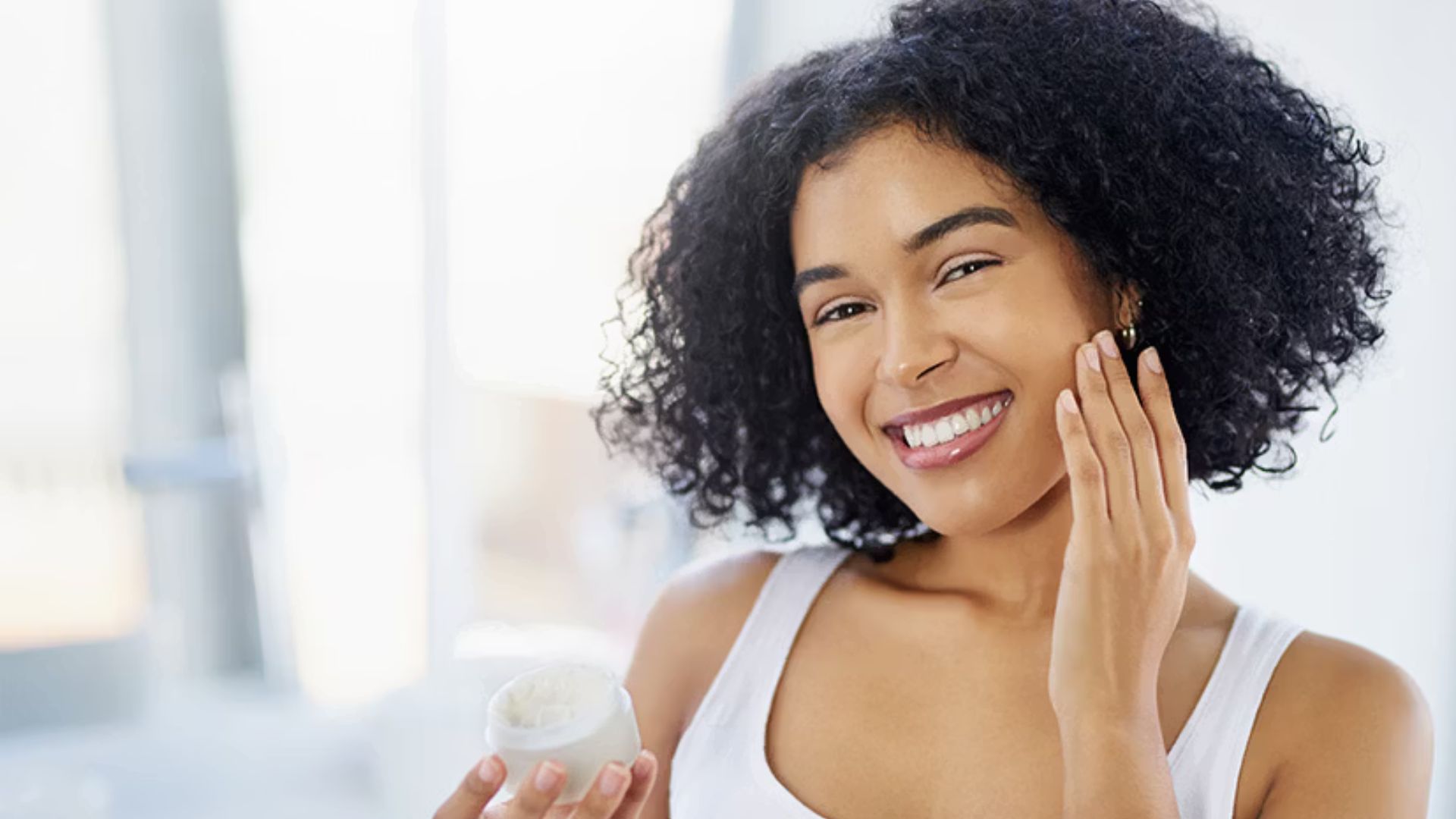 A smiling woman holds a jar of cream, showcasing her enthusiasm for the product.