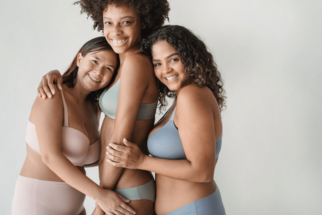 Three women in underwear pose together for a photo, showcasing confidence and camaraderie.