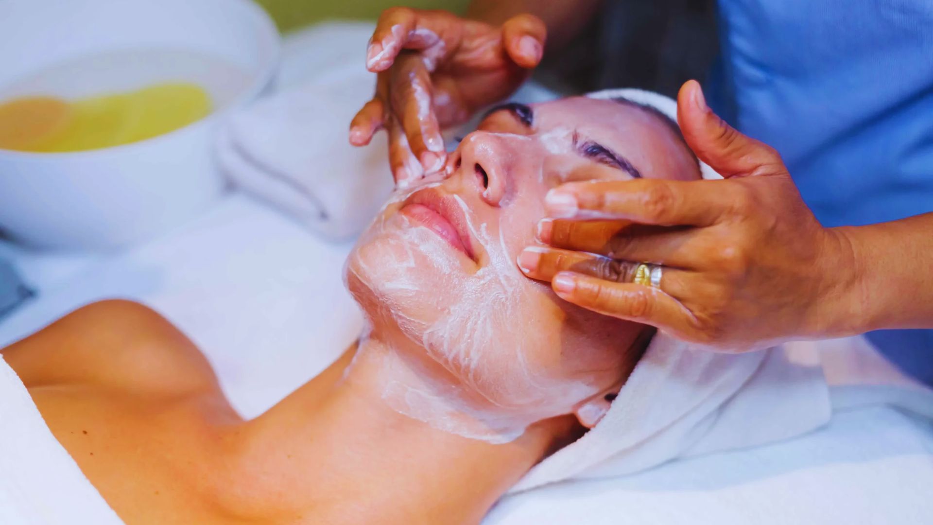 A woman receiving a facial treatment at a serene spa, surrounded by calming decor and soft lighting.