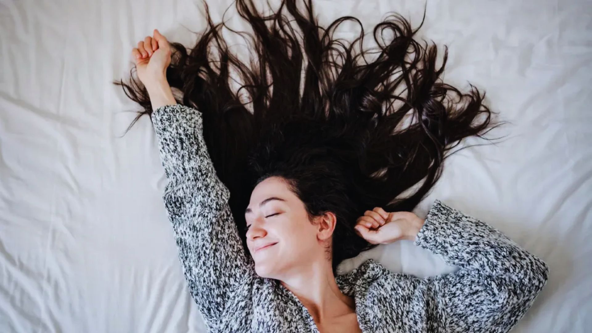 A woman lies on a bed, her hair flowing gracefully in the wind.