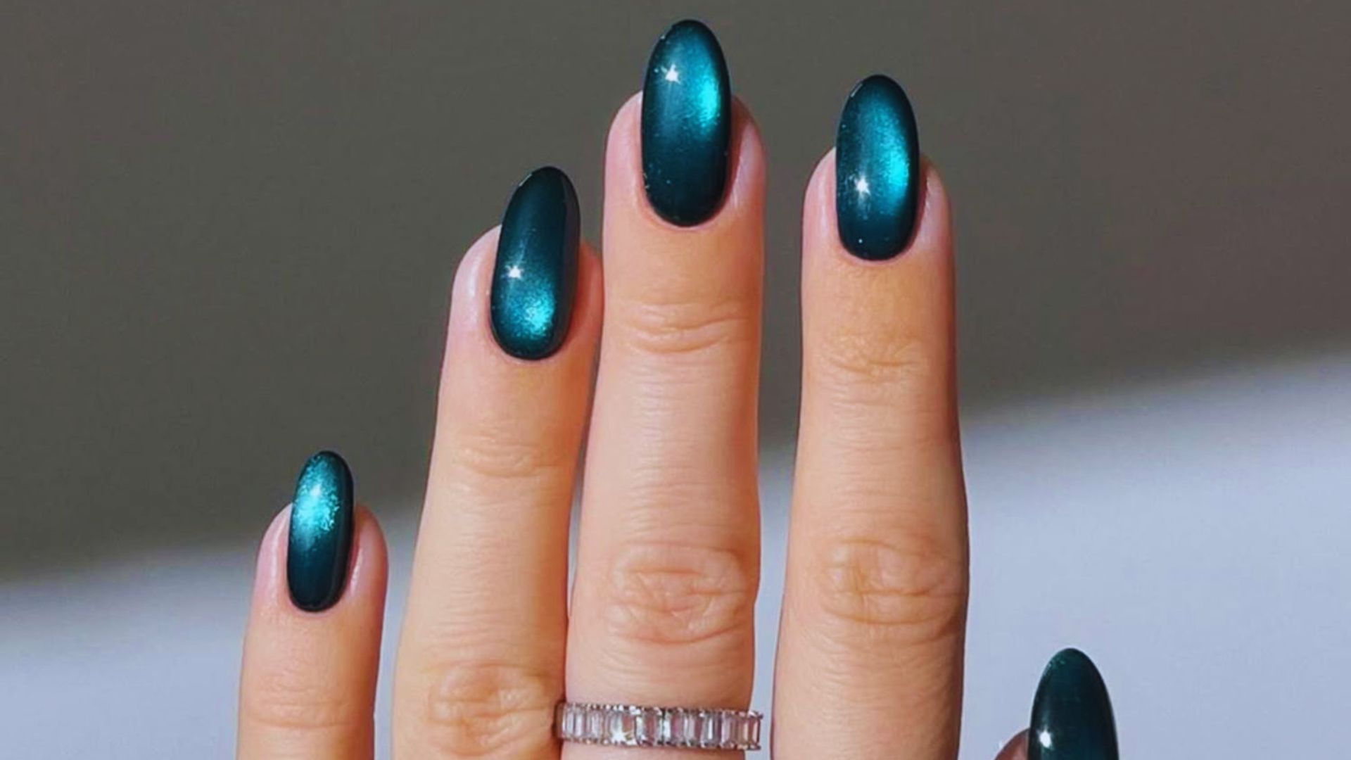 A close-up of a woman's hand with green nails adorned with a stylish ring.