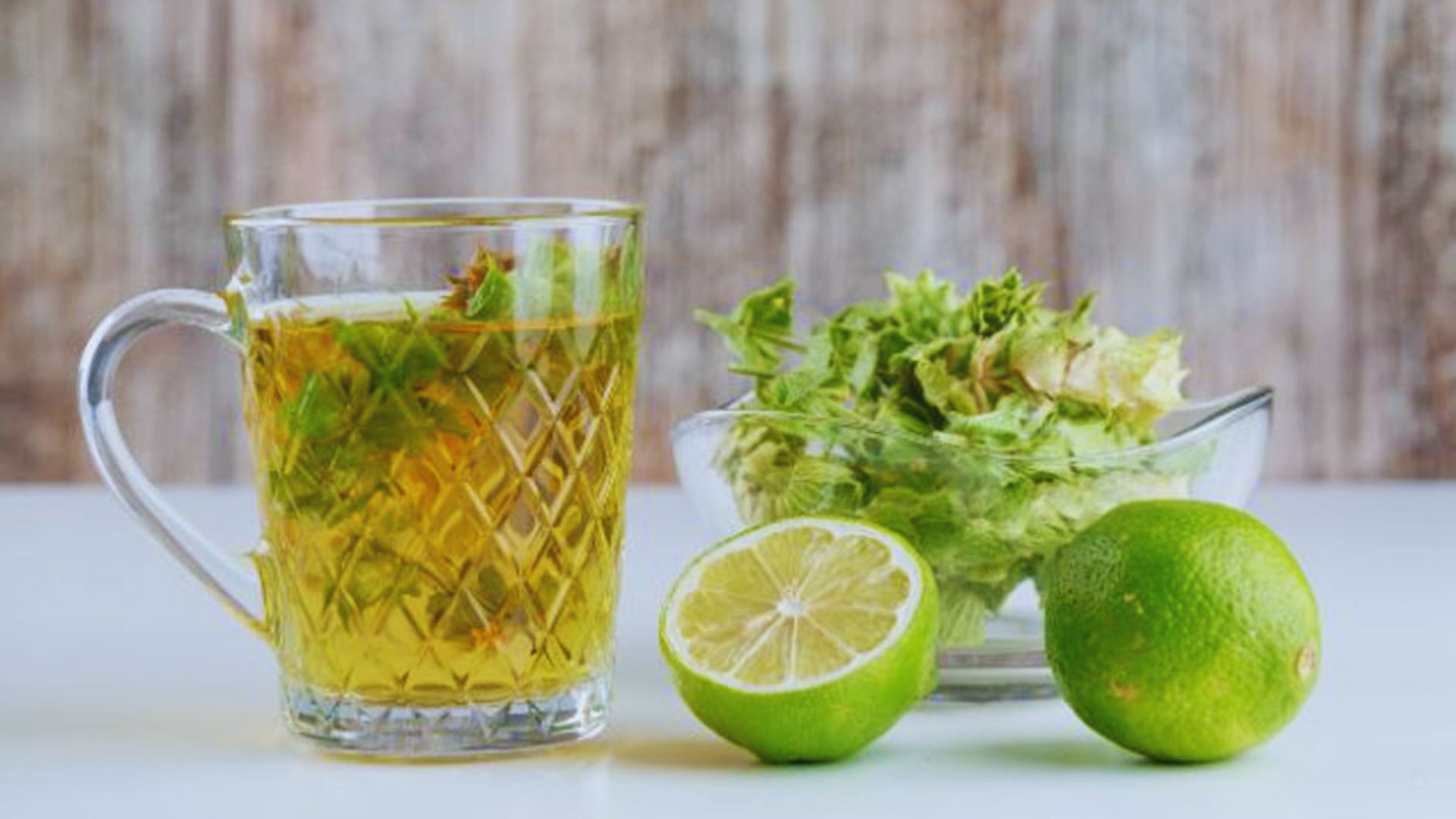 A glass of green tea garnished with lime slices and fresh lettuce leaves, showcasing a refreshing beverage.