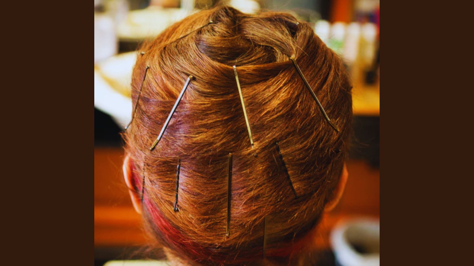 A woman with red hair is seated in a salon chair while a stylist works on her hair.
