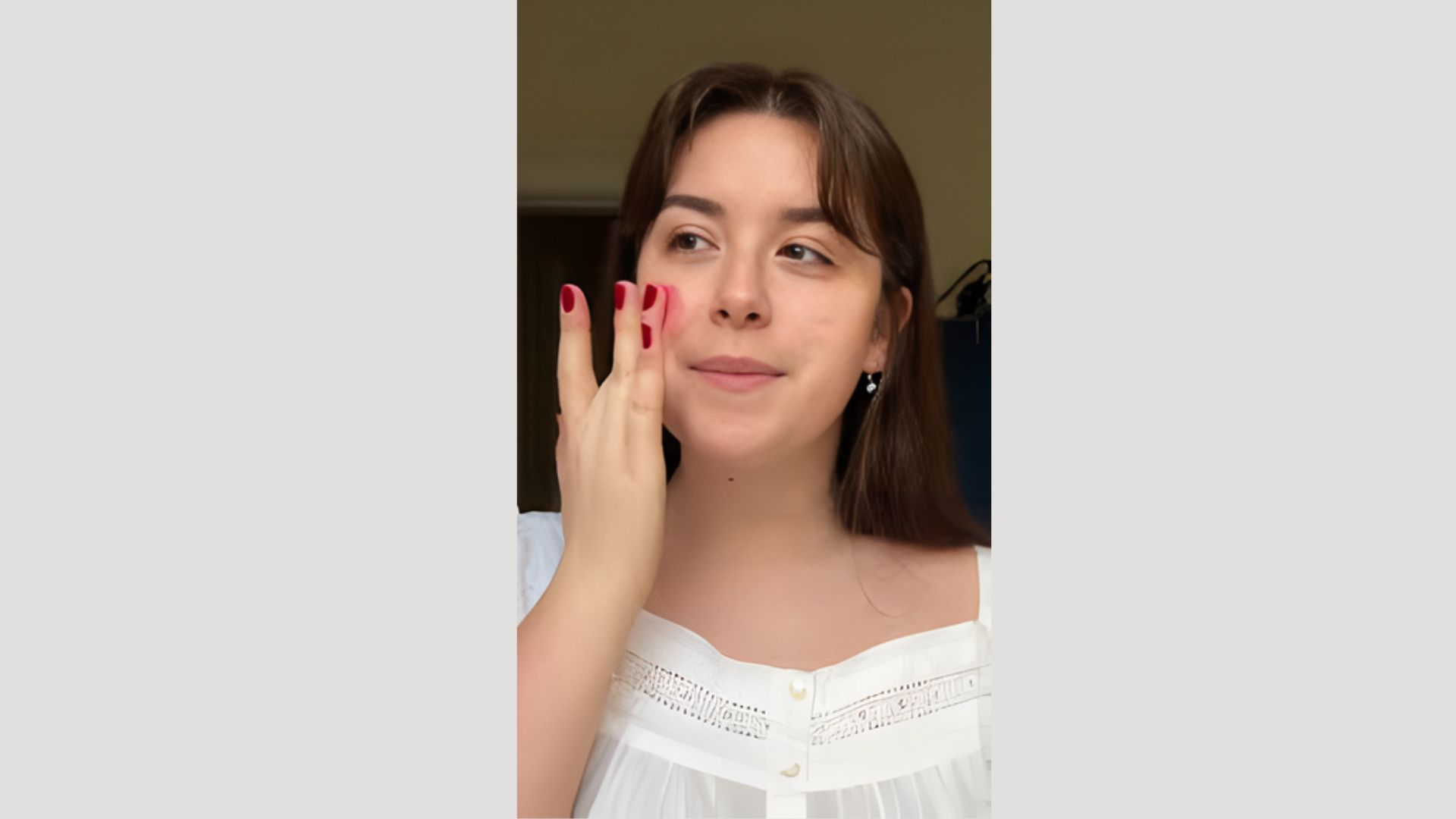 A woman with red nails and a white shirt is holding her face, expressing a thoughtful or contemplative emotion.