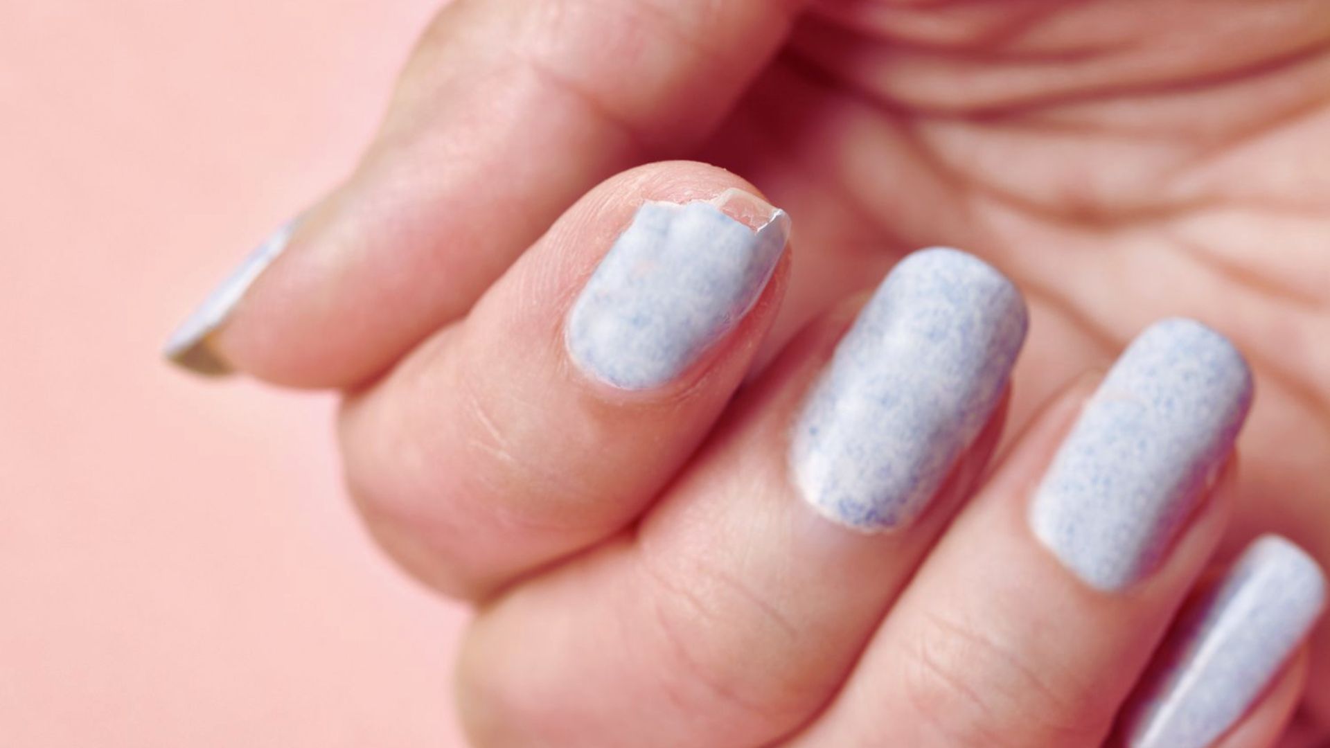 A person with blue nail polish holds a bottle of nail polish, showcasing their colorful manicure.
