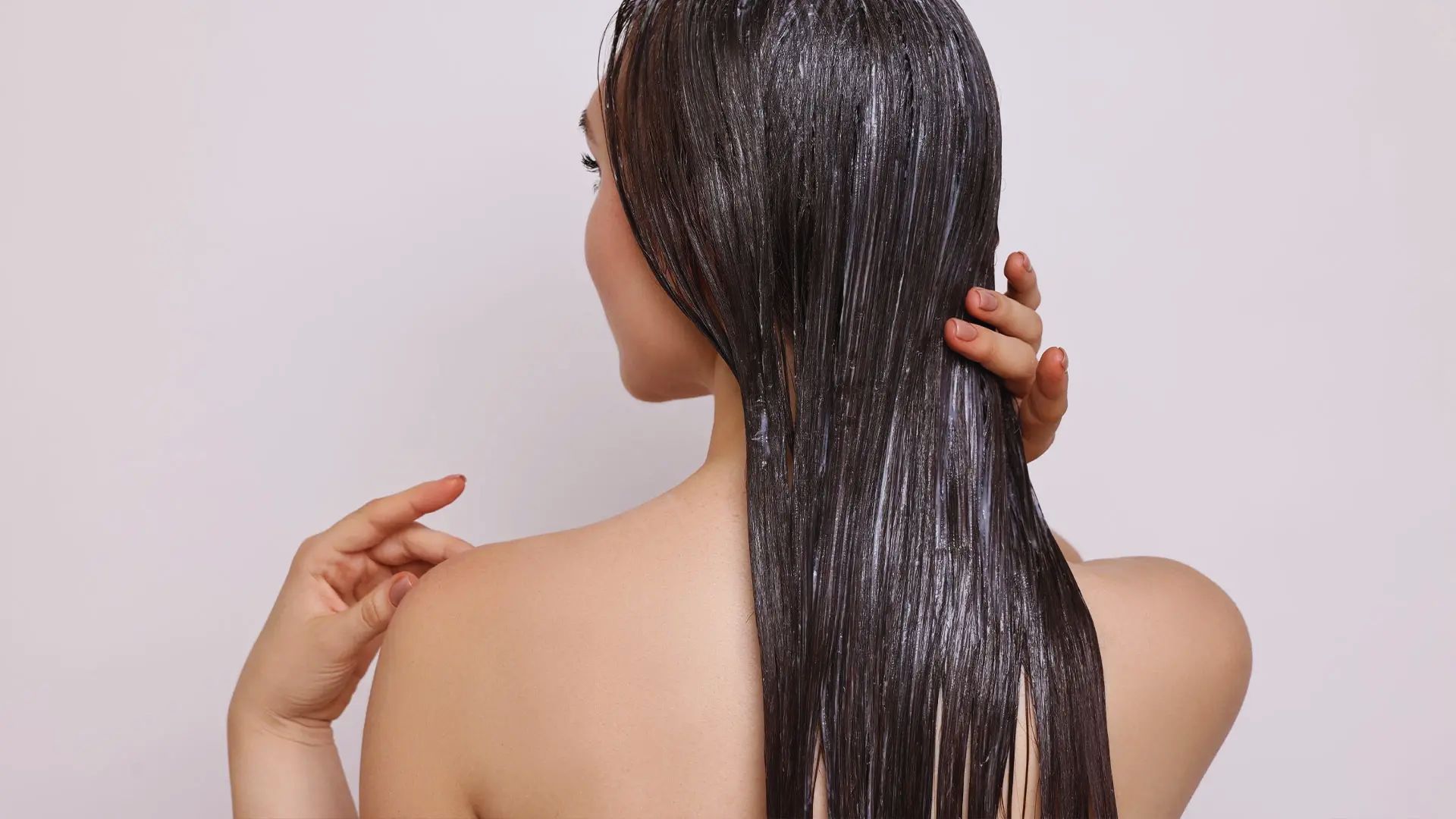 A woman with long black hair is gently combing her hair, focusing on smoothing and styling it.