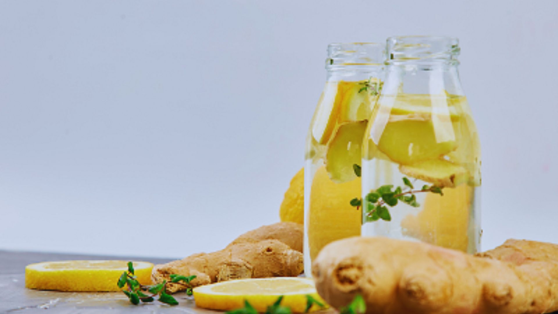 Two bottles of lemonade filled with ginger and garnished with fresh lemon slices.