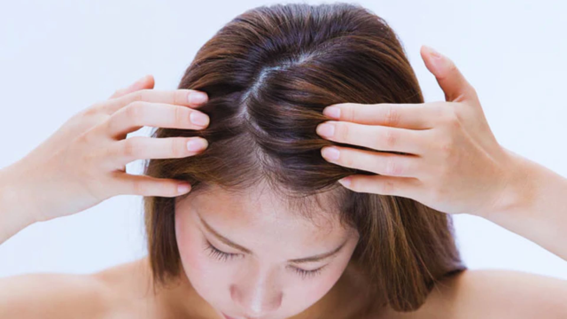A woman gently touches her hair with both hands, showcasing a moment of self-care and contemplation.