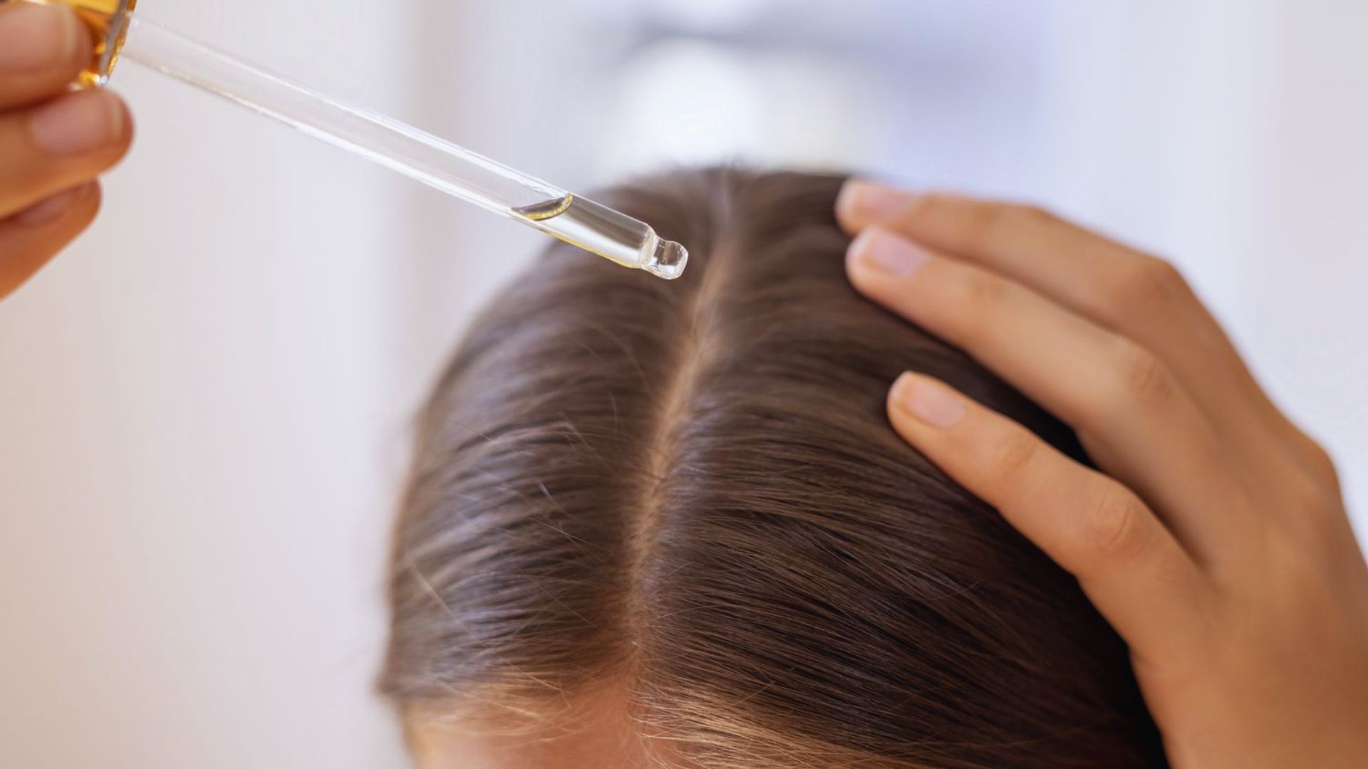 A woman applies hair treatment while combing her hair, focusing on enhancing its texture and shine.