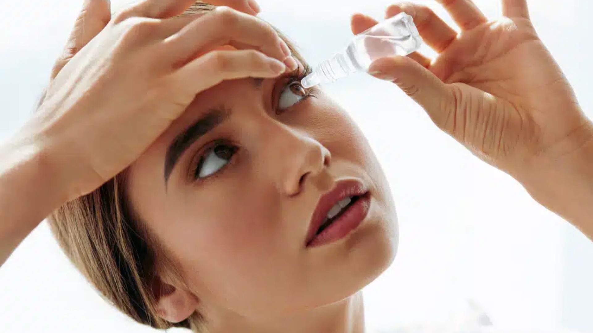 A woman applying mascara to her eyelashes in front of a mirror, focusing on her makeup routine.