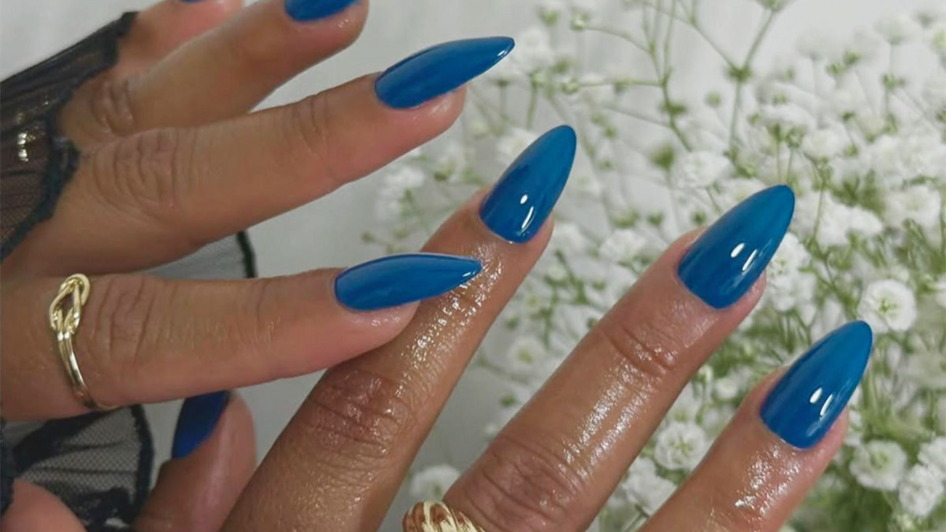 A woman displays her blue nails and a ring on her finger, showcasing her stylish manicure and jewelry.