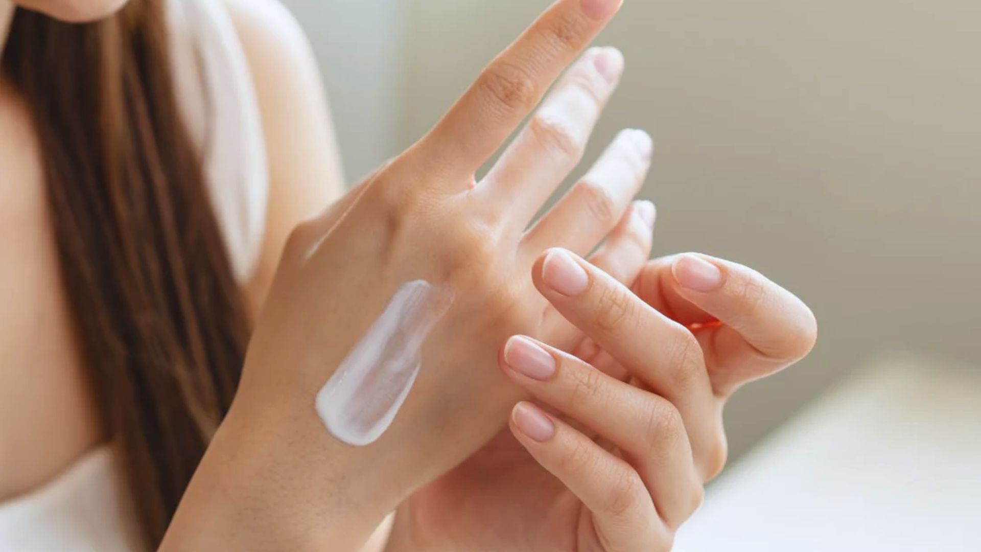 A woman applying moisturizing cream to her hands, focusing on skincare and hydration.