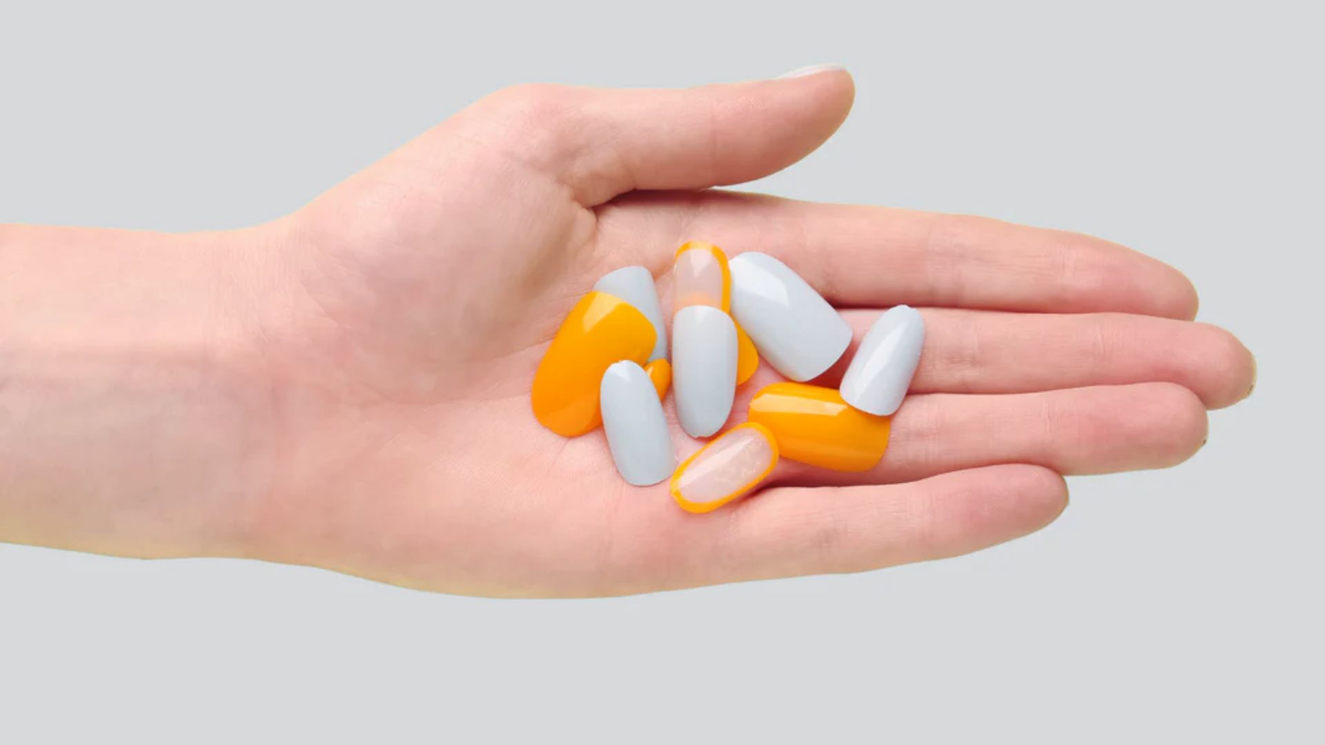 A hand holding various pills against a plain gray background.