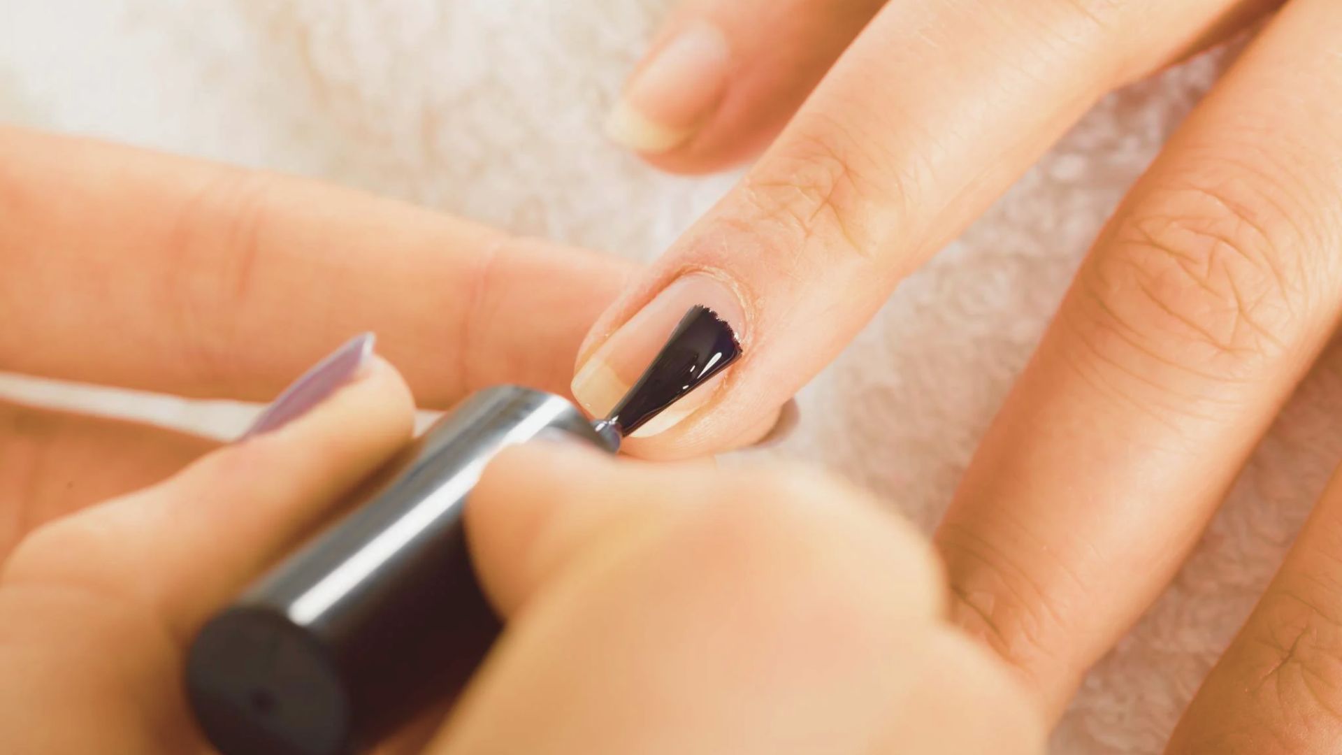 A woman is having her nails painted with glossy black polish at a nail salon.