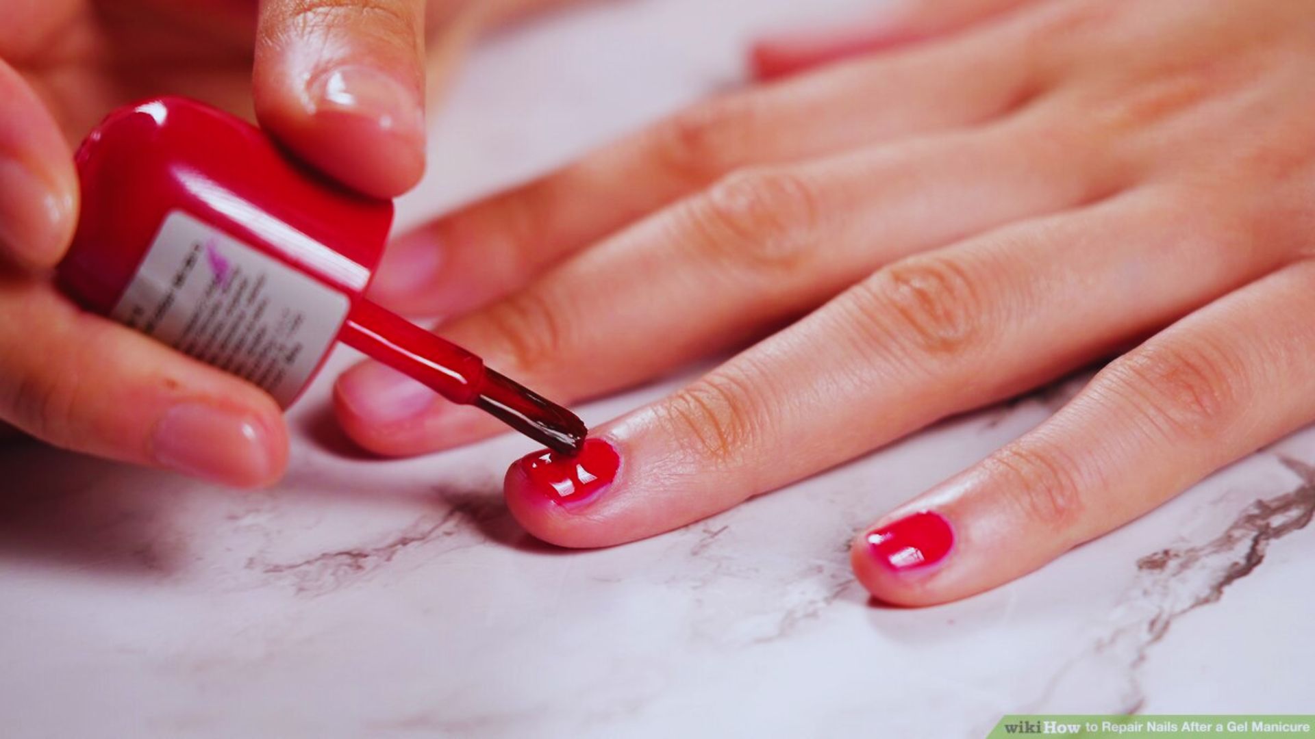A person applies bright red nail polish to their nails, focusing on achieving an even coat.