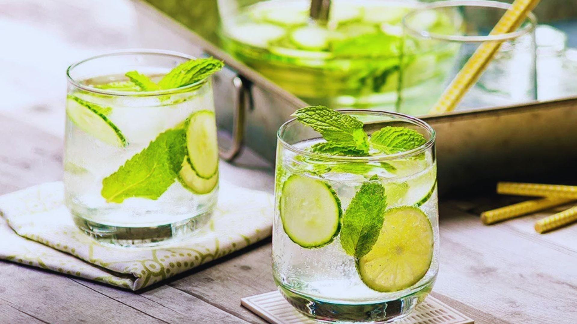 Two glasses of water infused with fresh mint and cucumber slices, placed on a wooden table.