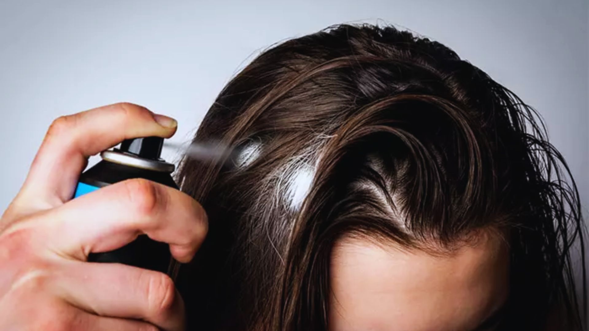 A woman applies hair spray to her damp hair, preparing to style it as it dries.