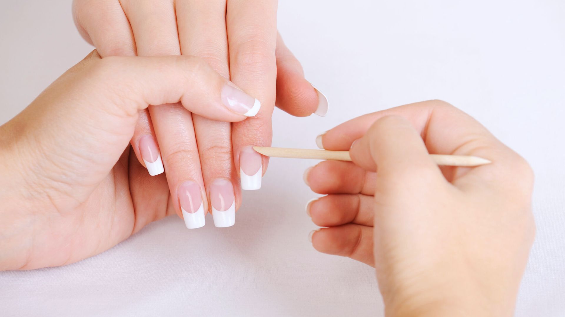 A woman applies a manicure using a nail brush, focusing on her nails with precision and care.